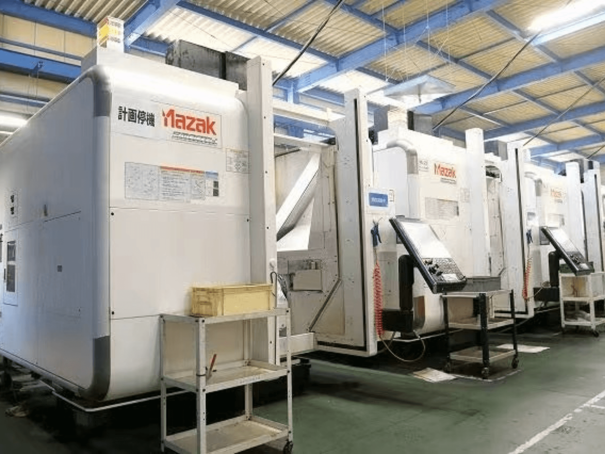 Mazak CNC machines in een fabrieksomgeving, zijaanzicht met bedieningspanelen en labels op witte behuizing.