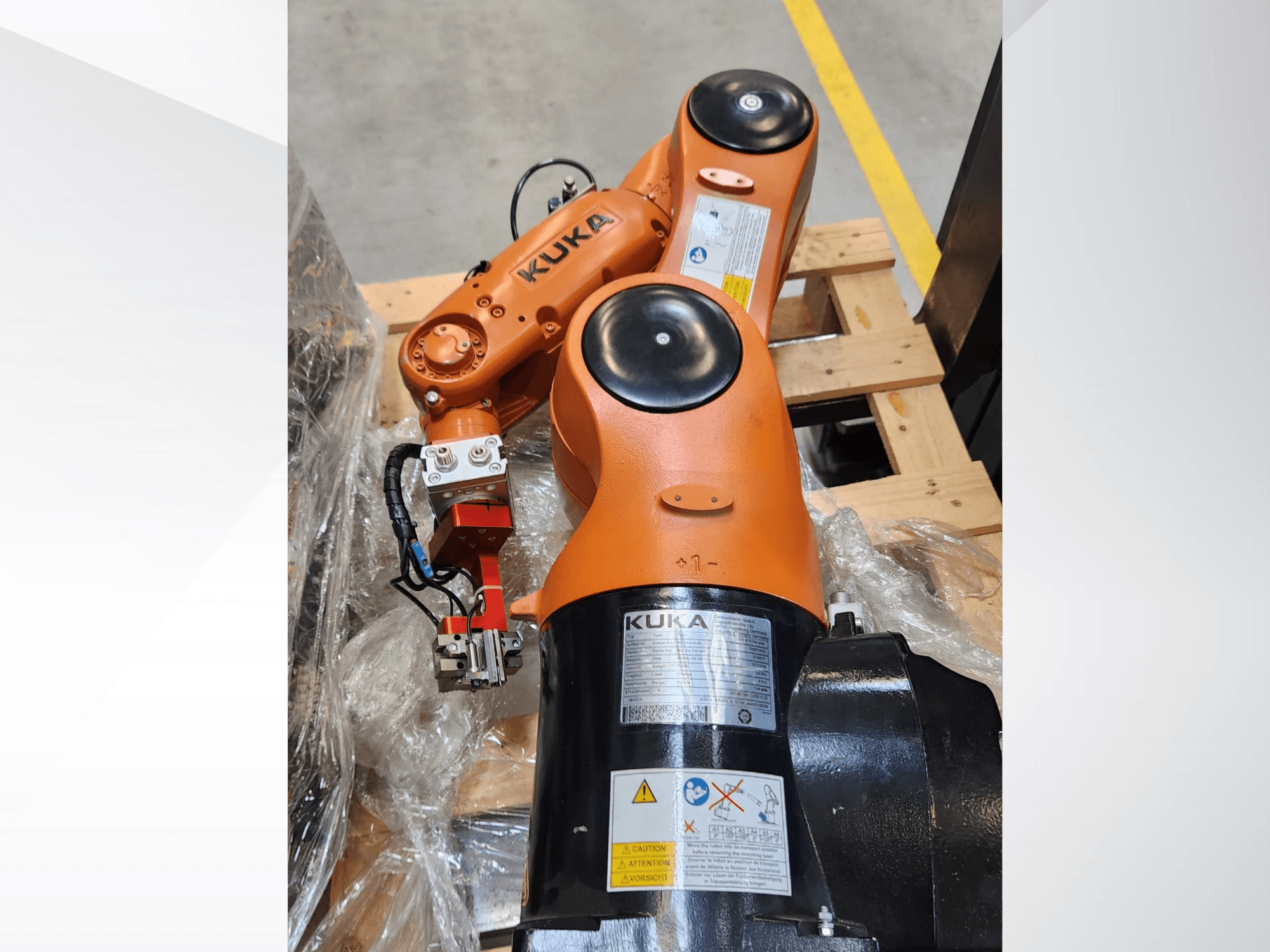 KUKA robotarm met oranje afwerking, zijaanzicht, met een grijper en besturingsbedrading op een houten pallet.