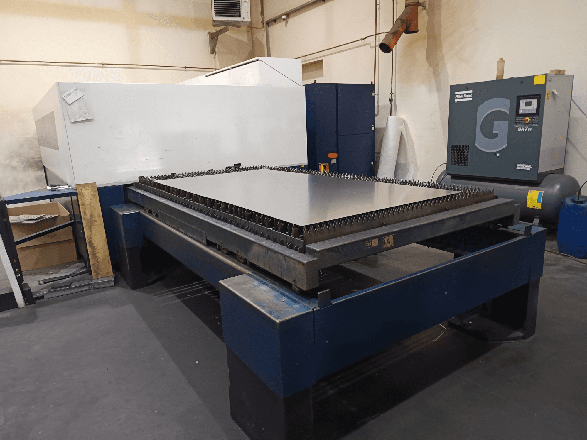 Industriële snijmachine met metalen tafel, vooraanzicht. Met scherpe randen, luchtcompressor rechts en stalen frame.