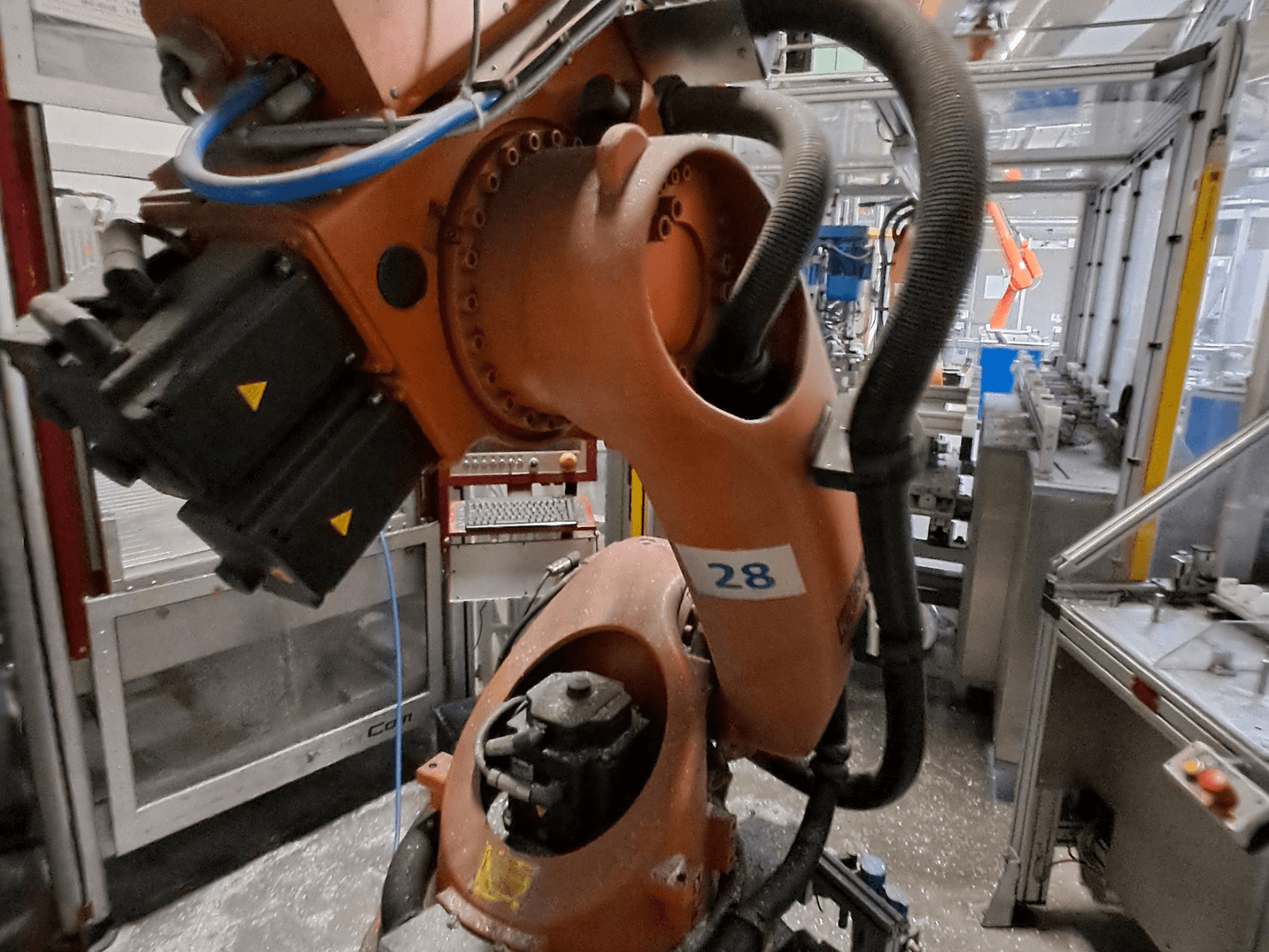 Close-up van de KUKA KR30-3-robotarm, met een oranje behuizing, voorzien van het nummer 28, waarop de motoren en bedrading vanuit een zijaanzicht te zien zijn.
