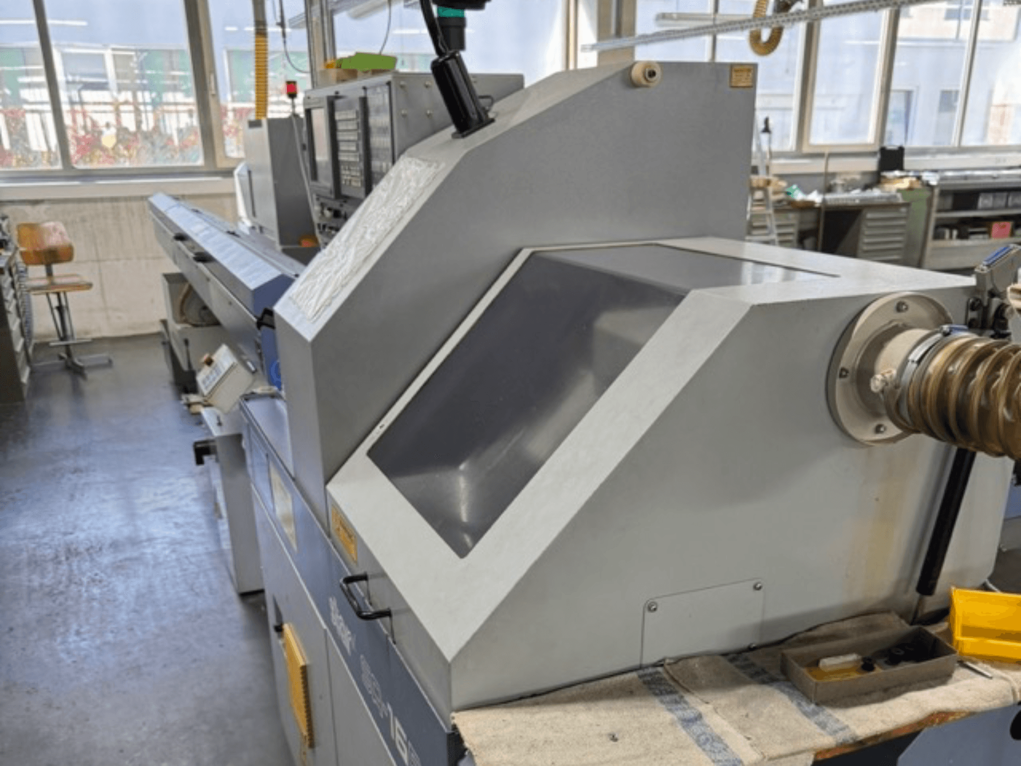 Grijze industriële machine gezien vanaf de zijkant, met een groot schuin paneel, bedieningsknoppen en een slangbevestiging.