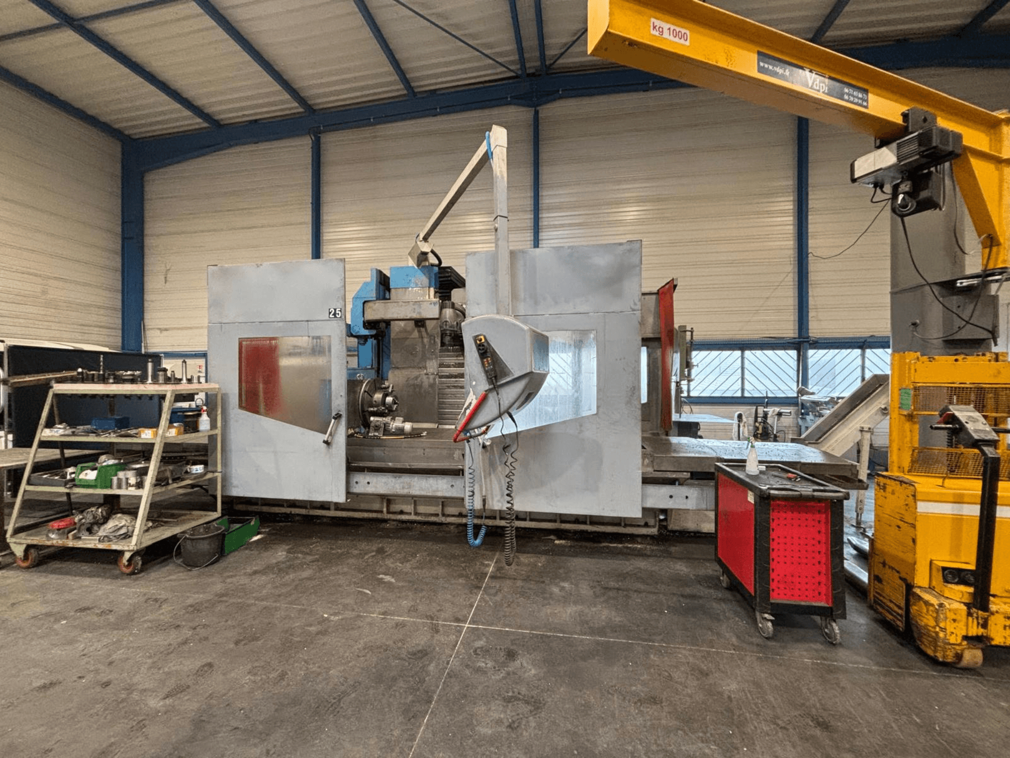 CNC freesmachine in zijaanzicht in een werkplaats; zichtbaar gereedschap en opbergplanken. Merk en model niet gespecificeerd.