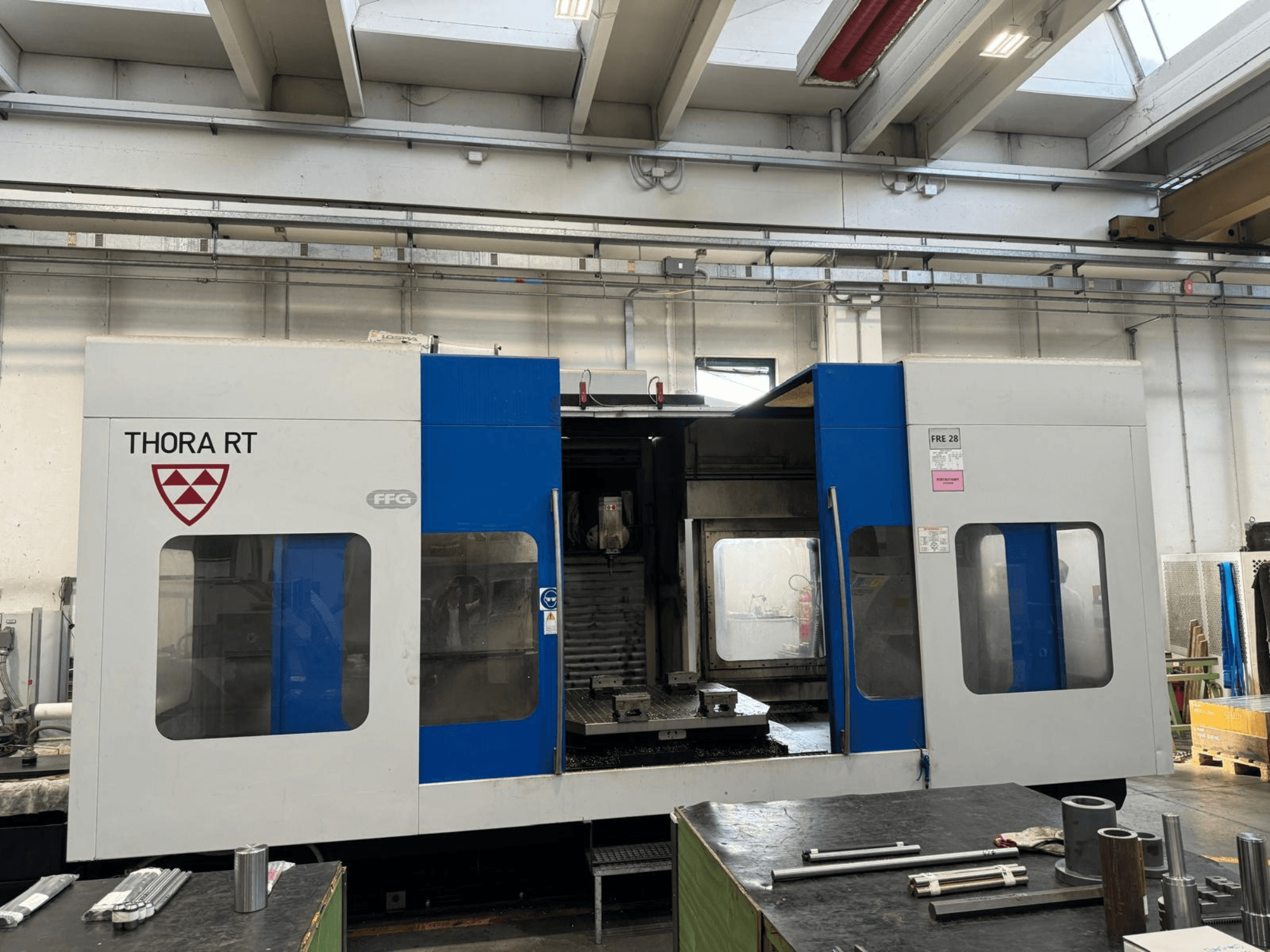THORA RT CNC machine gezien vanaf de voorkant, met een blauw-witte buitenkant, transparante ramen en gemonteerde gereedschappen.