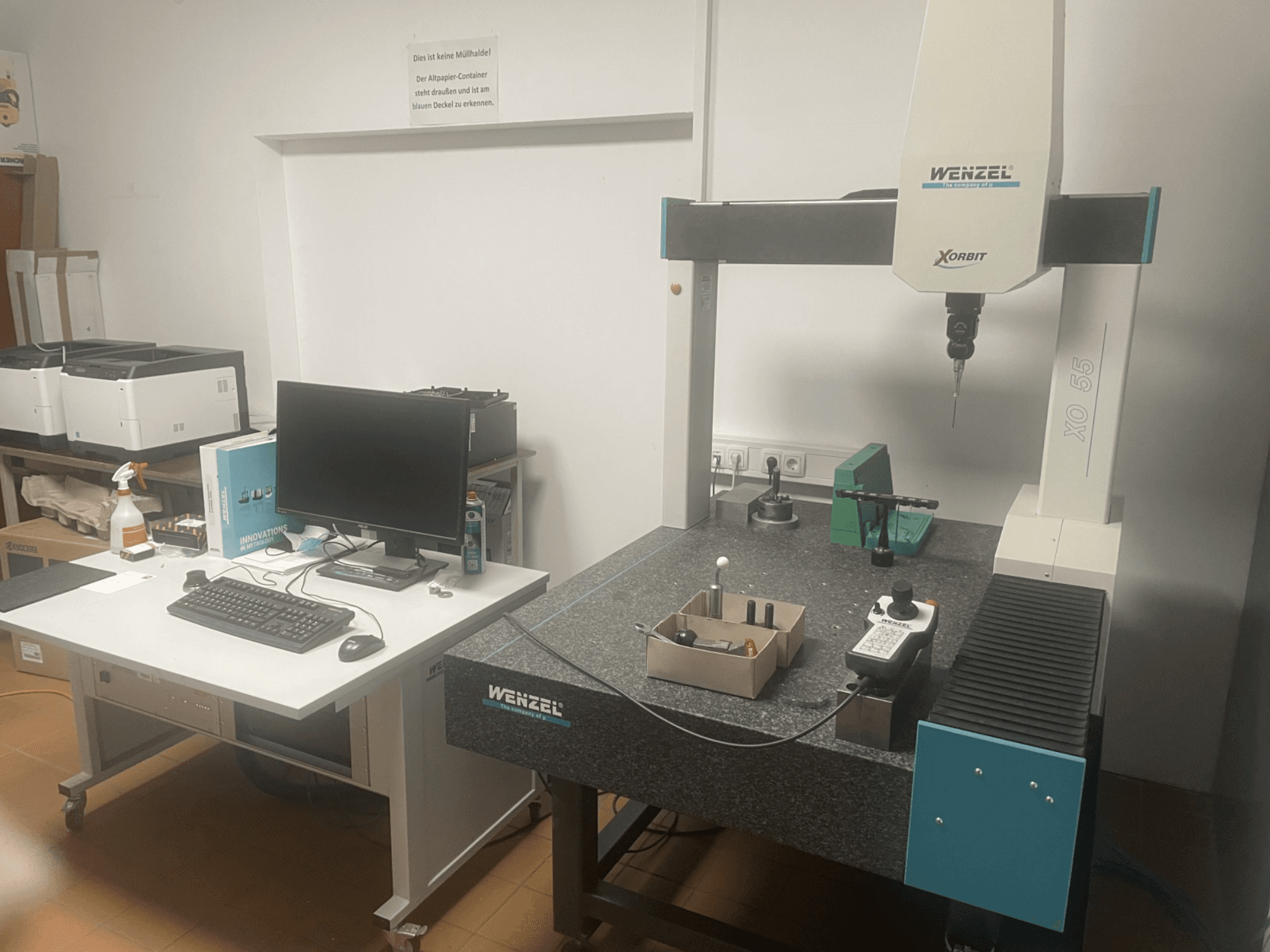 Wenzel XO 55 coördinatenmeetmachine met groene gereedschappen op een granieten tafel, gezien vanaf de voorkant met een computerstation.