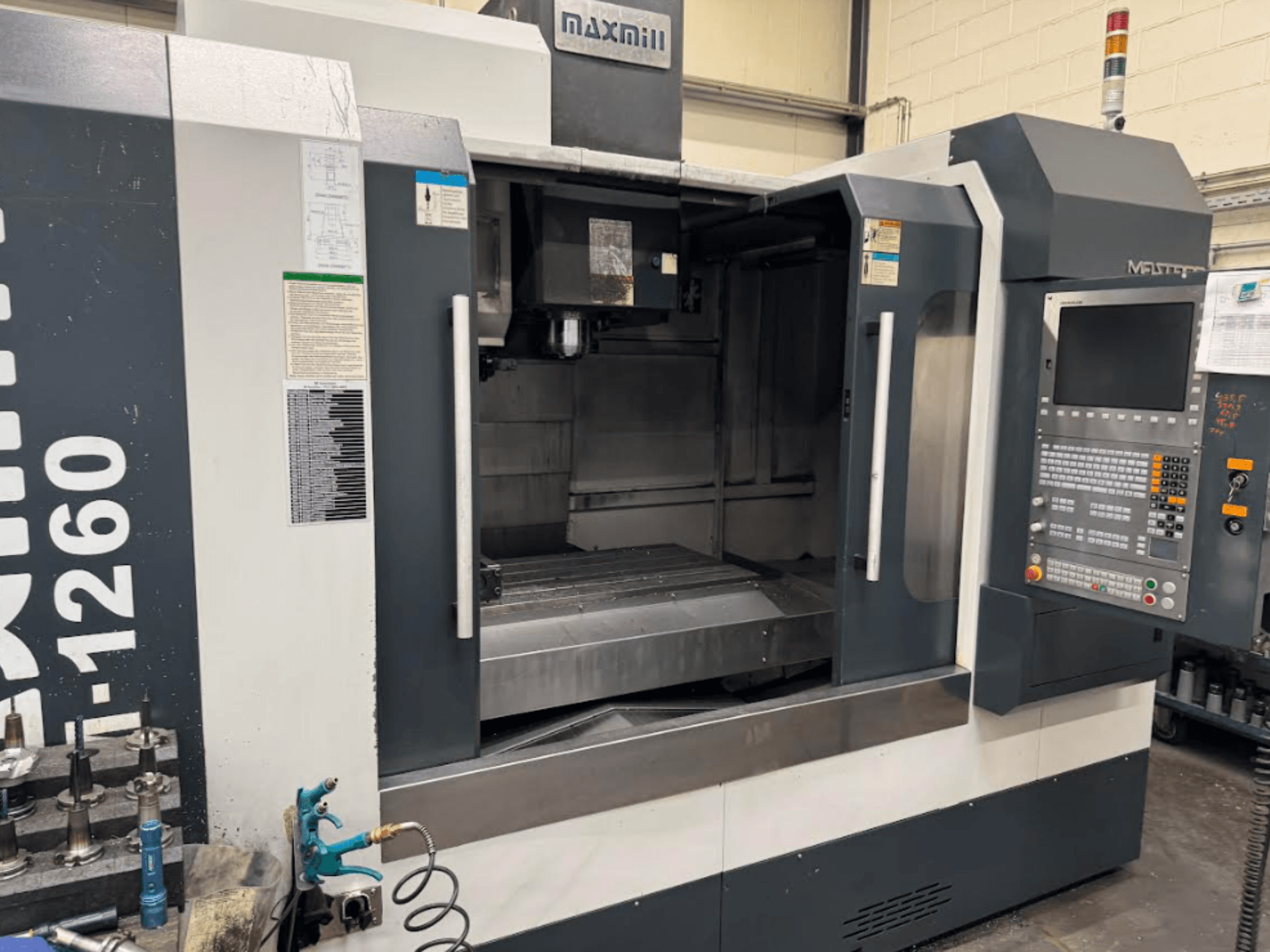 Maxmill CNC freesmachine, model M-1260, vooraanzicht met lege werkruimte met bedieningspaneel en bedieningsinstructies.