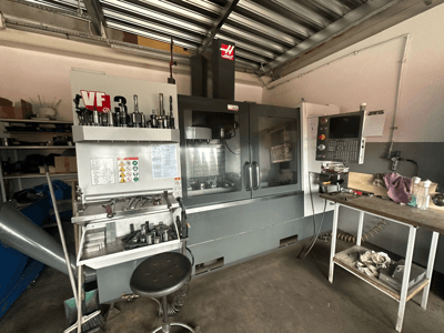Haas VF-3 CNC machine in werkplaats, vooraanzicht met gereedschappen en bedieningselementen op aangrenzende tafel, met weergave van technische interface en veiligheidsinformatie.