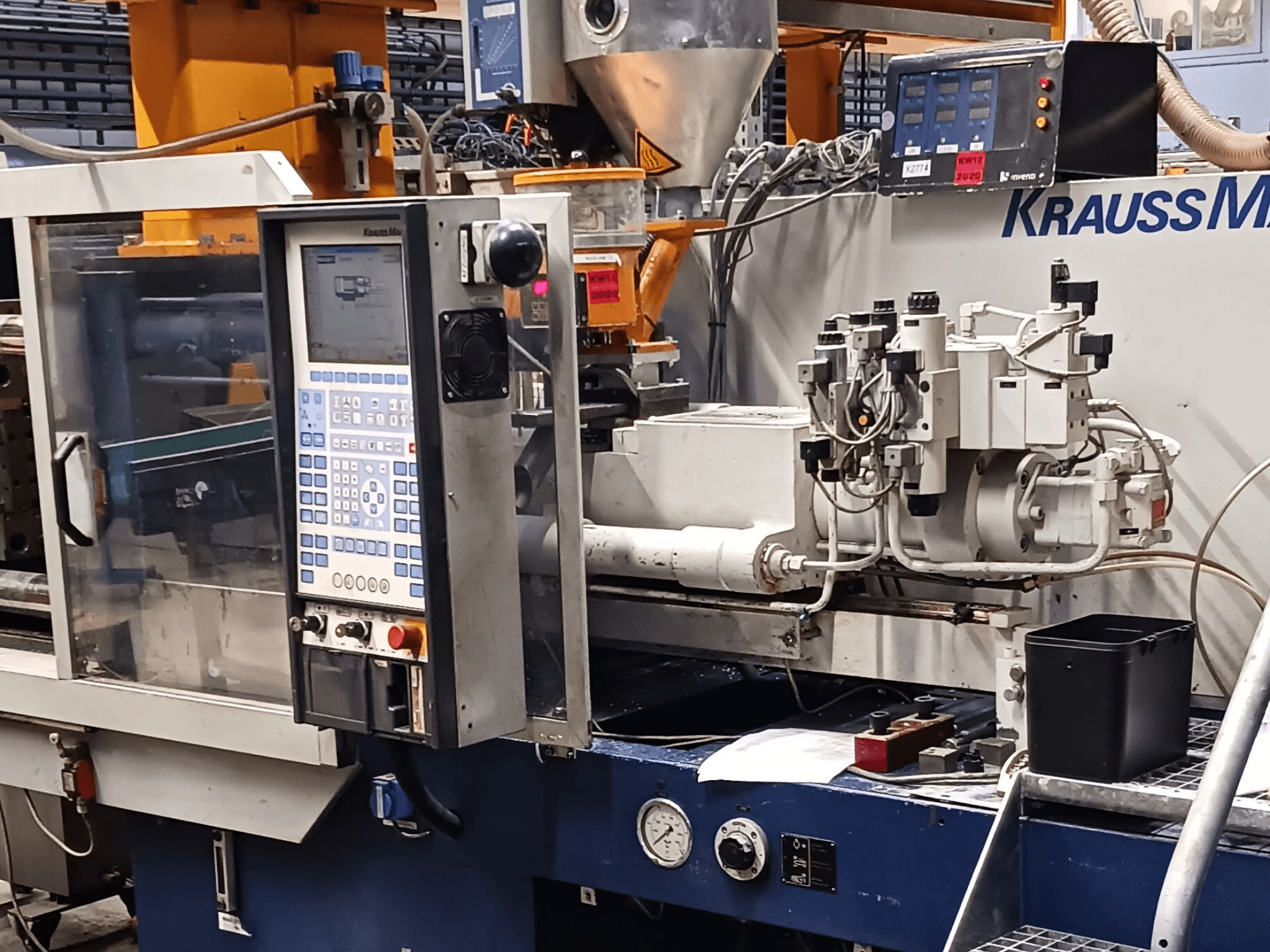 Spuitgietmachine van KraussMaffei met bedieningspaneel, hydraulische eenheden en gereedschappen op de voorgrond, vooraanzicht.