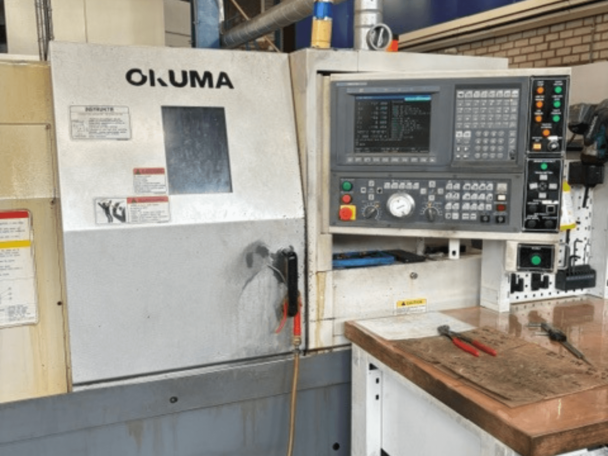 Vooraanzicht van de Okuma ES-L10II horizontale draaimachine, met bedieningspaneel, display en werkruimte met gereedschap.