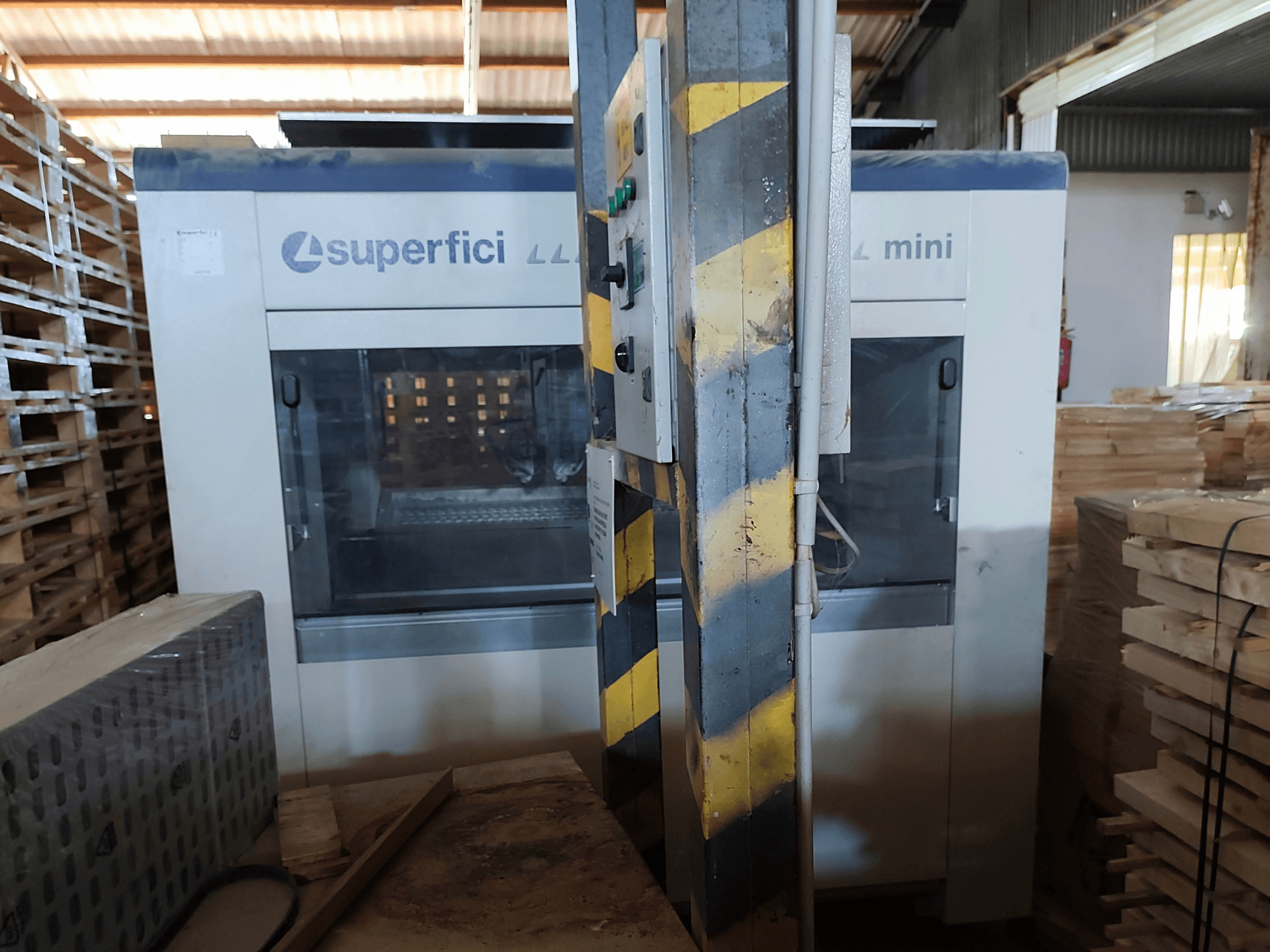 De SCM Superfici Mini-houtafwerkingsmachine in vooraanzicht, met het bedieningspaneel en de houten pallets eromheen.