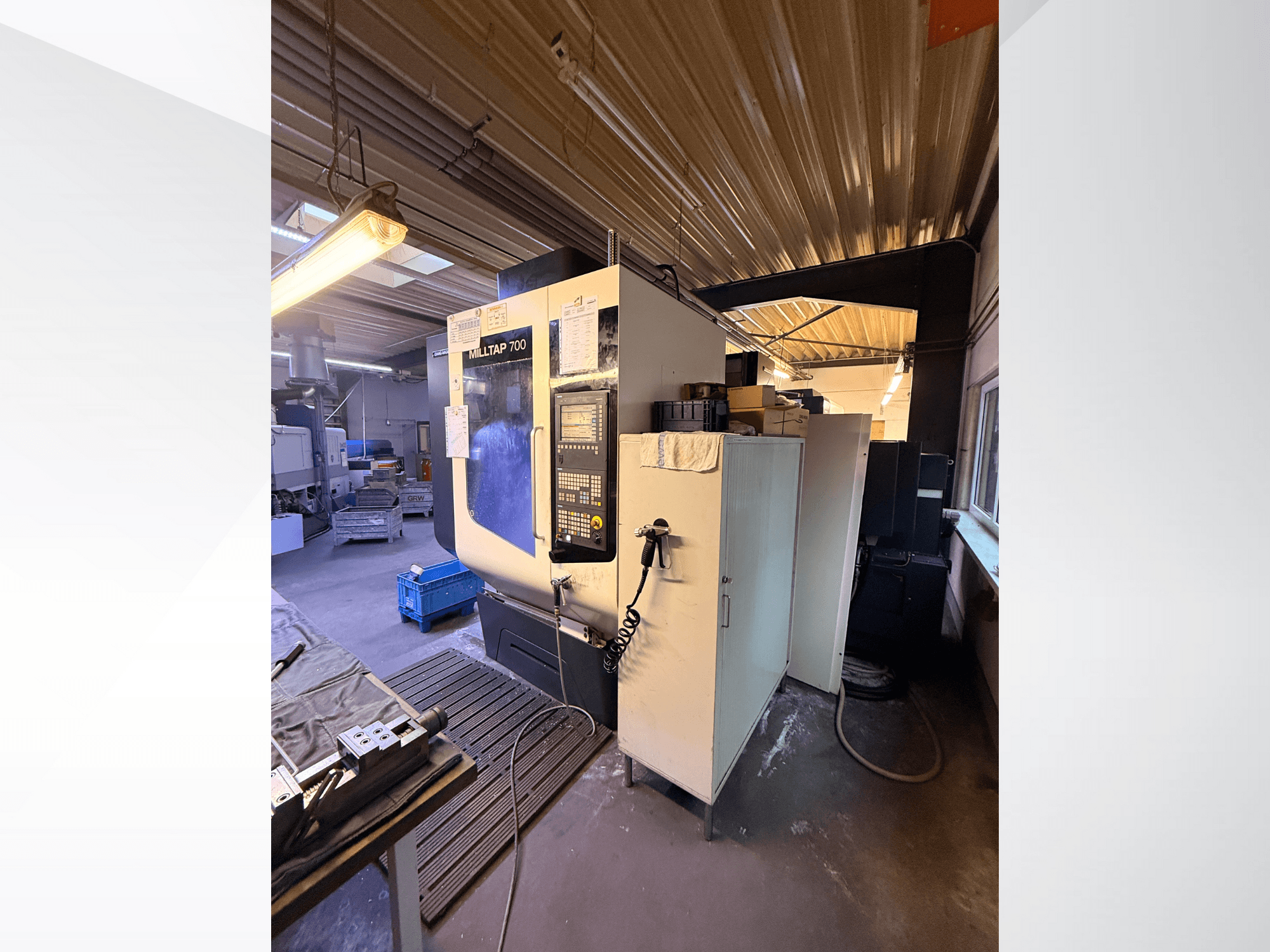 Milltap 700 CNC machine in werkplaats; vooraanzicht toont bedieningspaneel, gereedschaprekken en opslagruimtes met verlichting erboven.