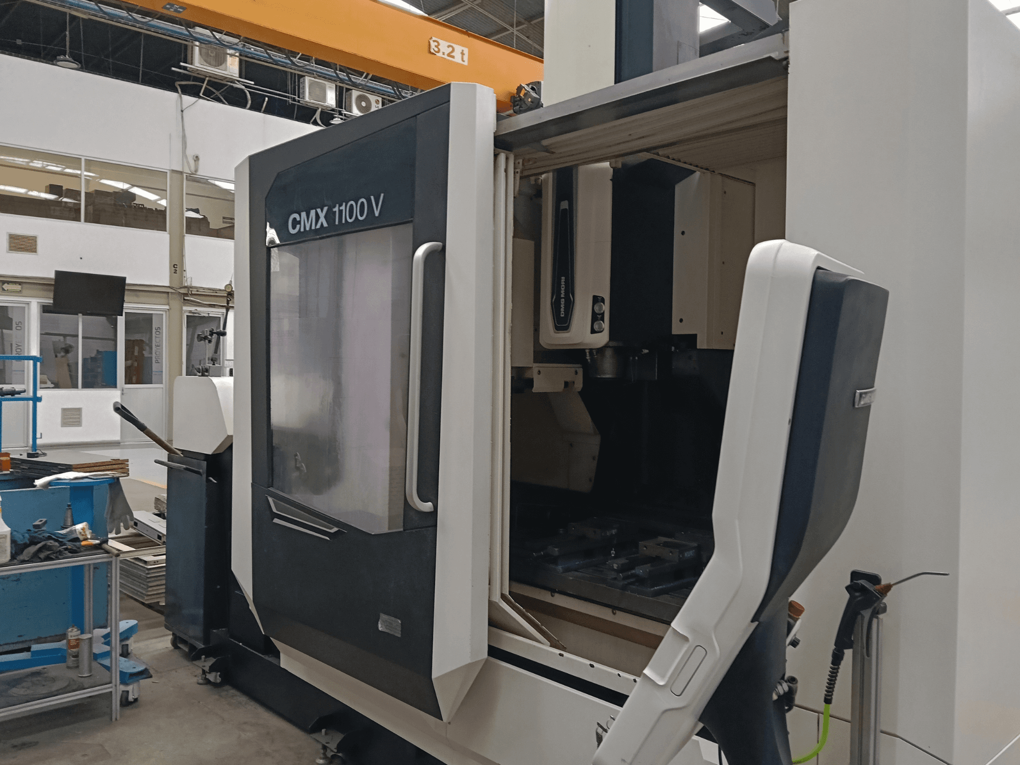 DMG MORI CMX 1100 V verticaal bewerkingscentrum, vooraanzicht met geopende deur en de opstelling van de gereedschappen in een industriële ruimte.