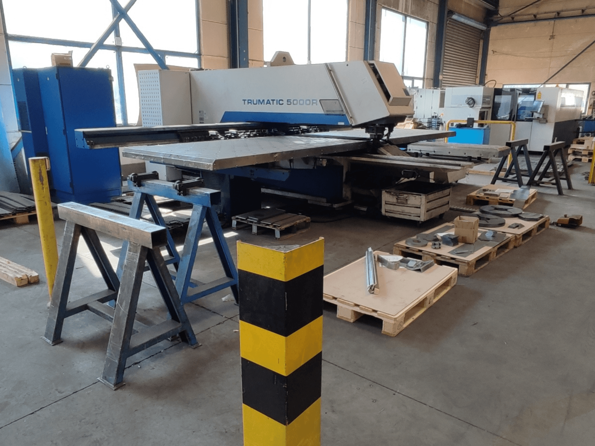 TRUMPF Trumatic 5000 R CNC-ponsmachine in een werkplaats, zijaanzicht met gereedschap en materialen op pallets ernaast.