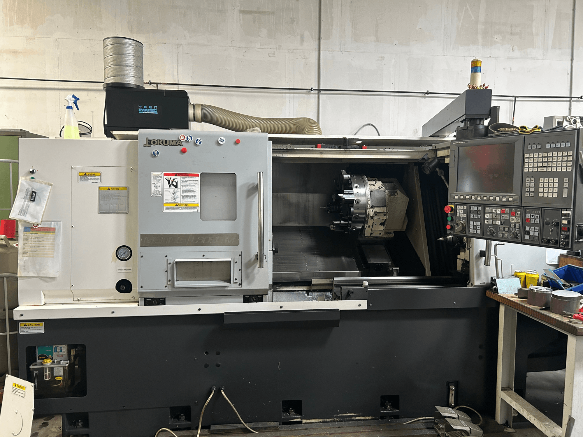 Vooraanzicht van een Okuma Genos L300E-M horizontale draaimachine met bedieningspaneel, zichtbare spindel en diverse instelgereedschappen.