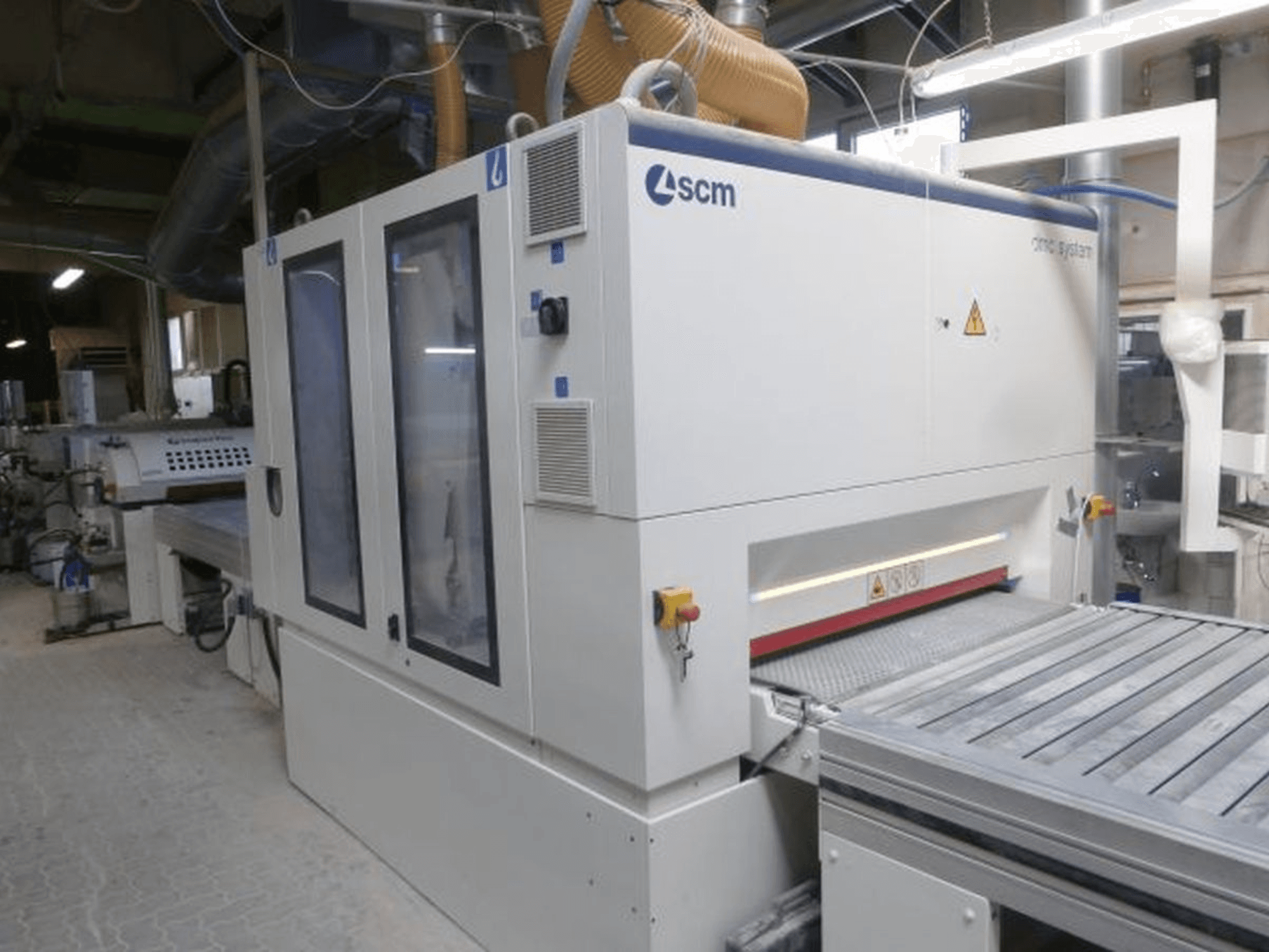 Bandschuurmachine SCM DMC SY TC 1350 in een werkplaats, zijaanzicht met bedieningspaneel en schuurvlak met veiligheidsvoorzieningen.