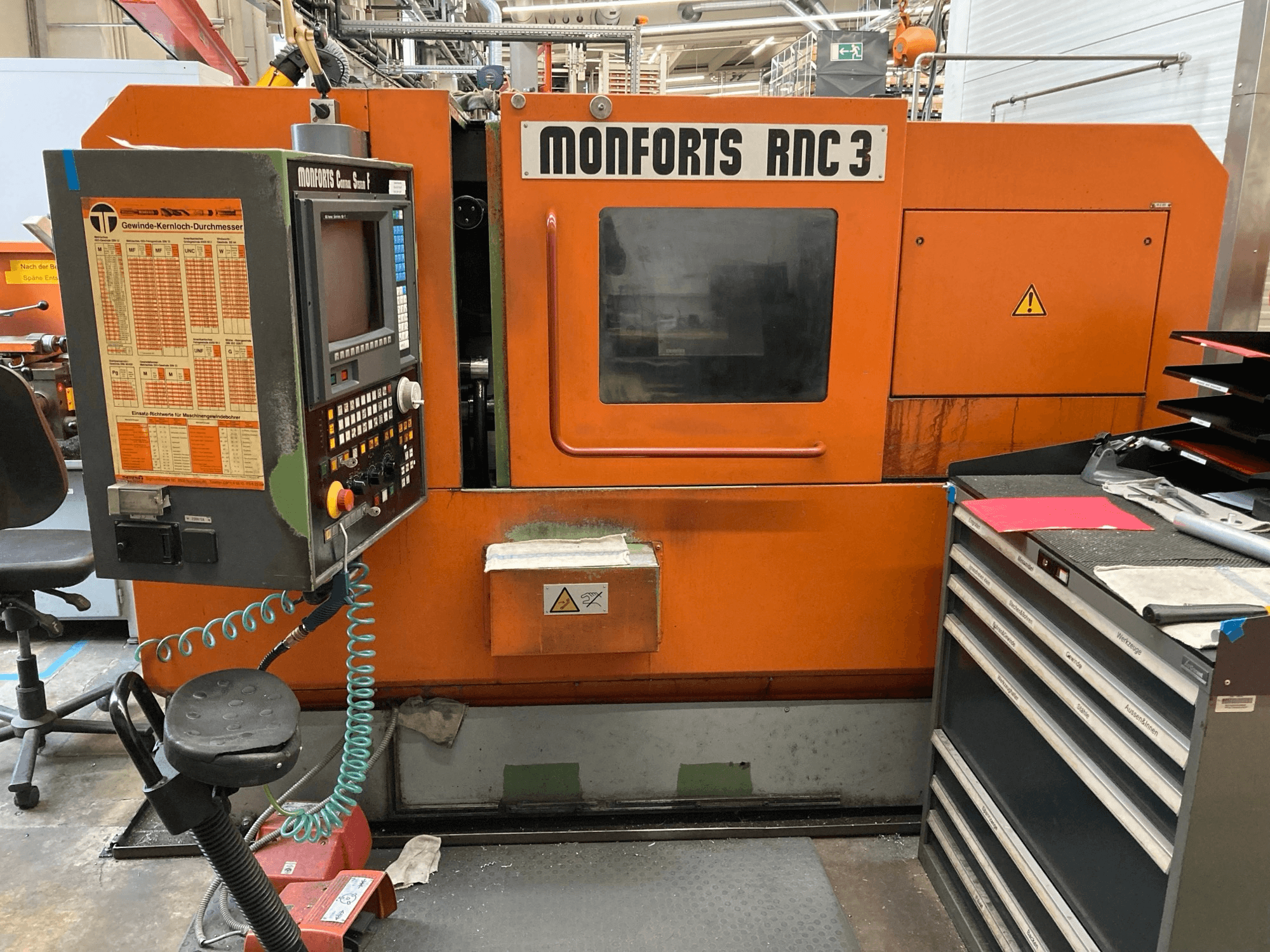 Monforts RNC 3 machine in oranje en zwart, vooraanzicht, met bedieningspaneel en diverse gereedschapslades.