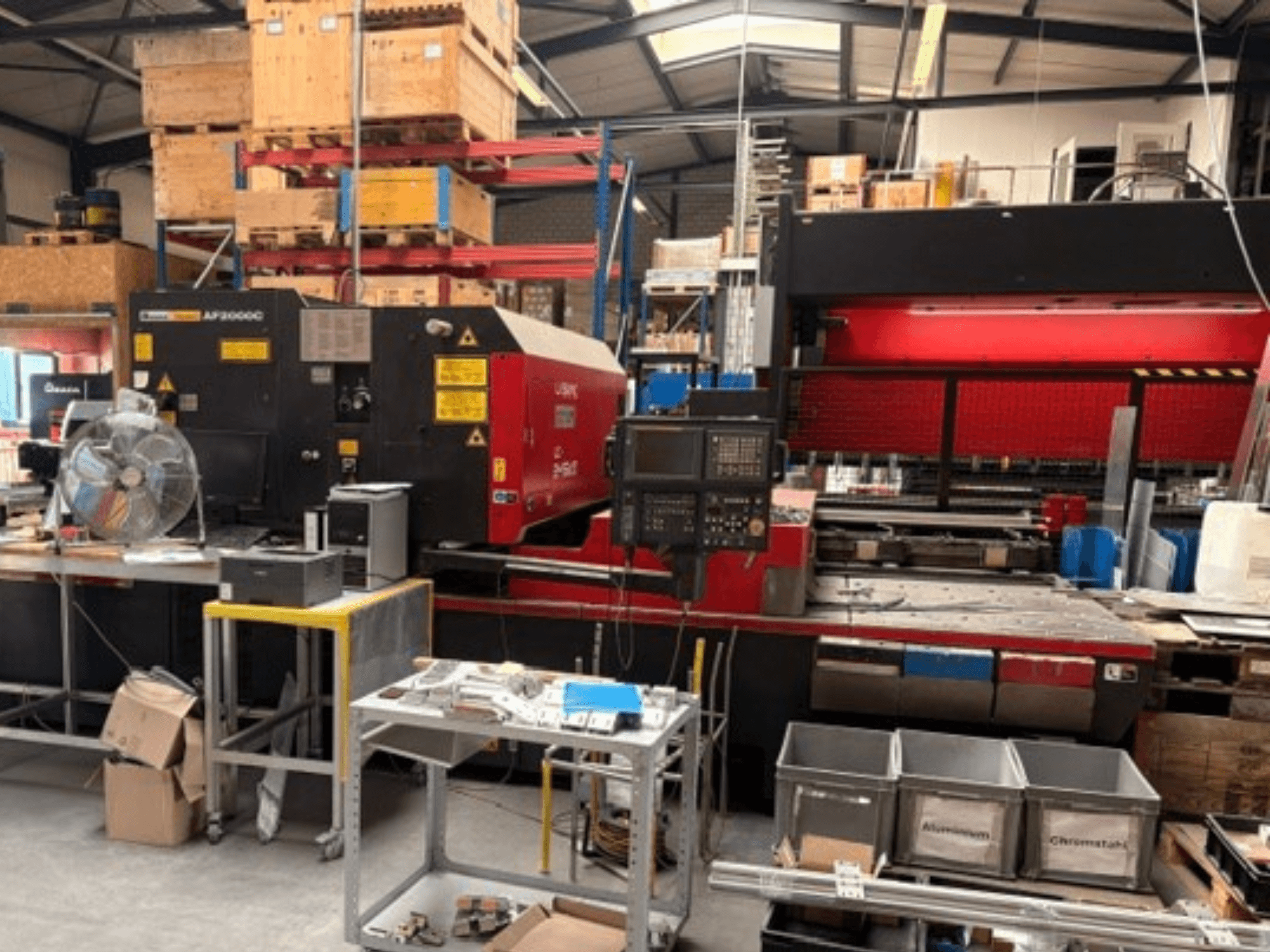 AMADA LC-2415αIII CO₂-lasersnijmachine in een werkplaatsomgeving, met een vooraanzicht, het bedieningspaneel en de werkruimte.