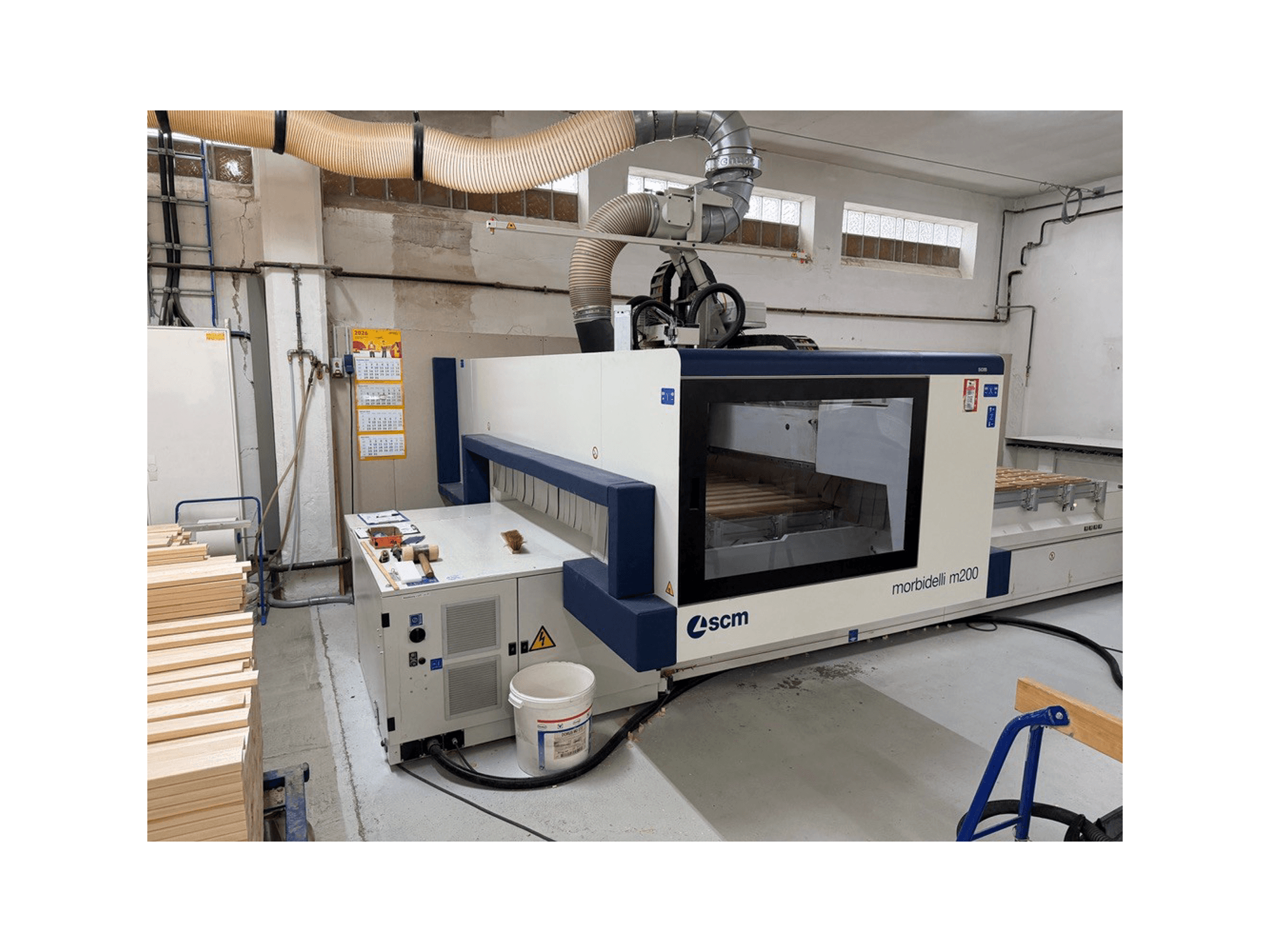 SCM Morbidelli M200F CNC-bewerkingscentrum in een werkplaats, zijaanzicht met stukken hout op de tafel en een ventilatiesysteem erboven.