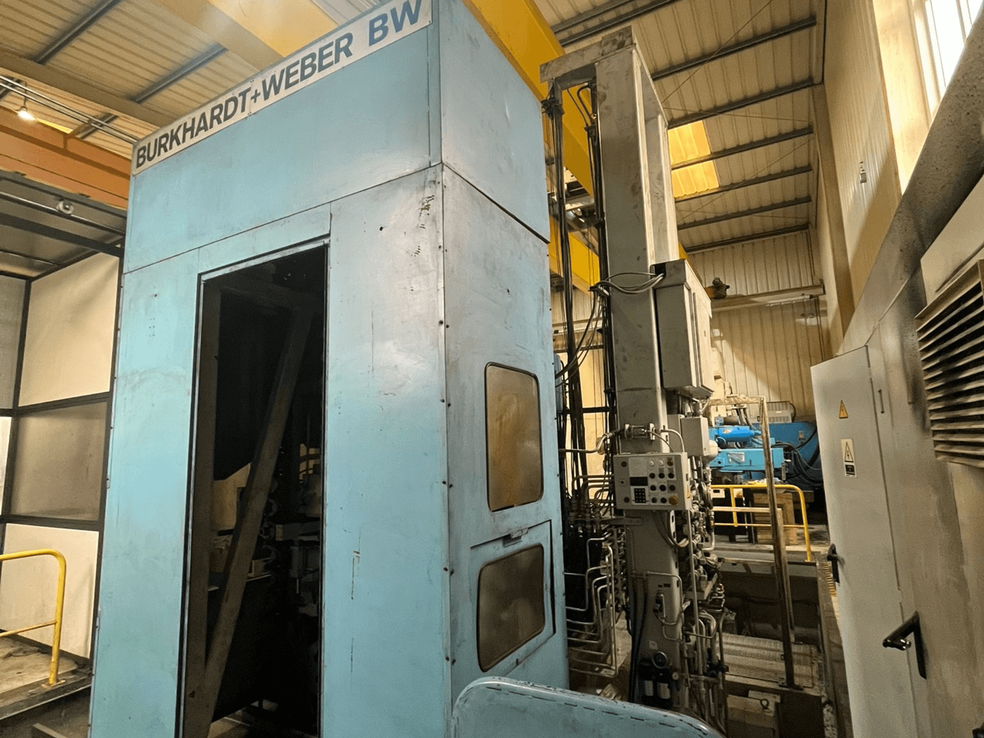 Burkhardt-Weber MC100 horizontaal bewerkingscentrum, zijaanzicht met blauwe behuizing en bedieningspaneel met zichtbare leidingen.