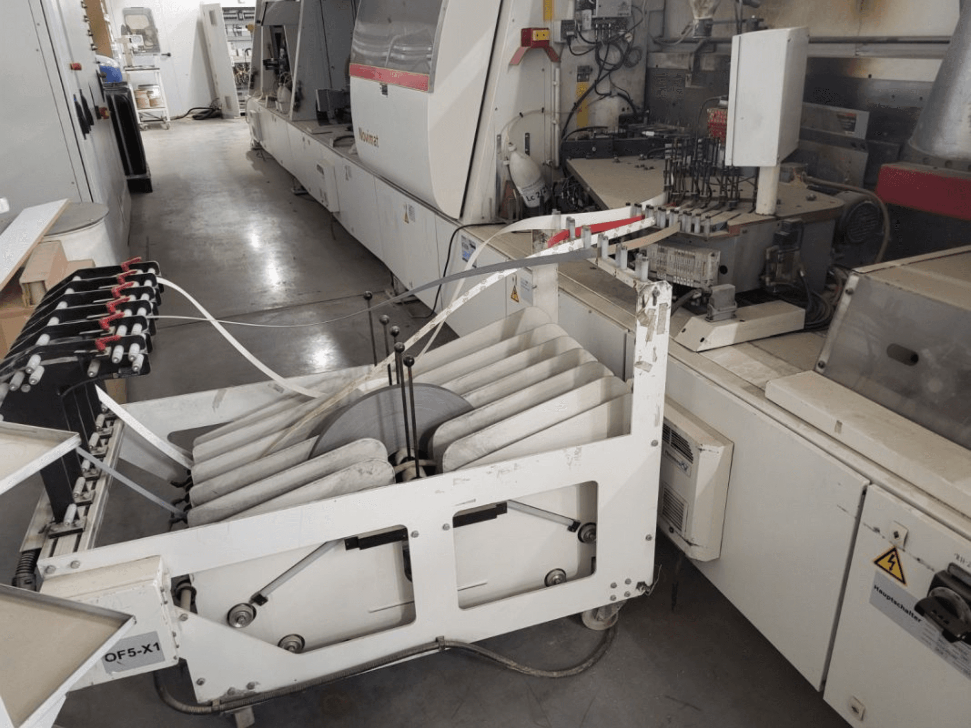 IMA Novimat/I/680/650/R3 kantenaanlijmmachine, zijaanzicht met invoerrollen en bedieningspaneel in een werkplaatsomgeving.