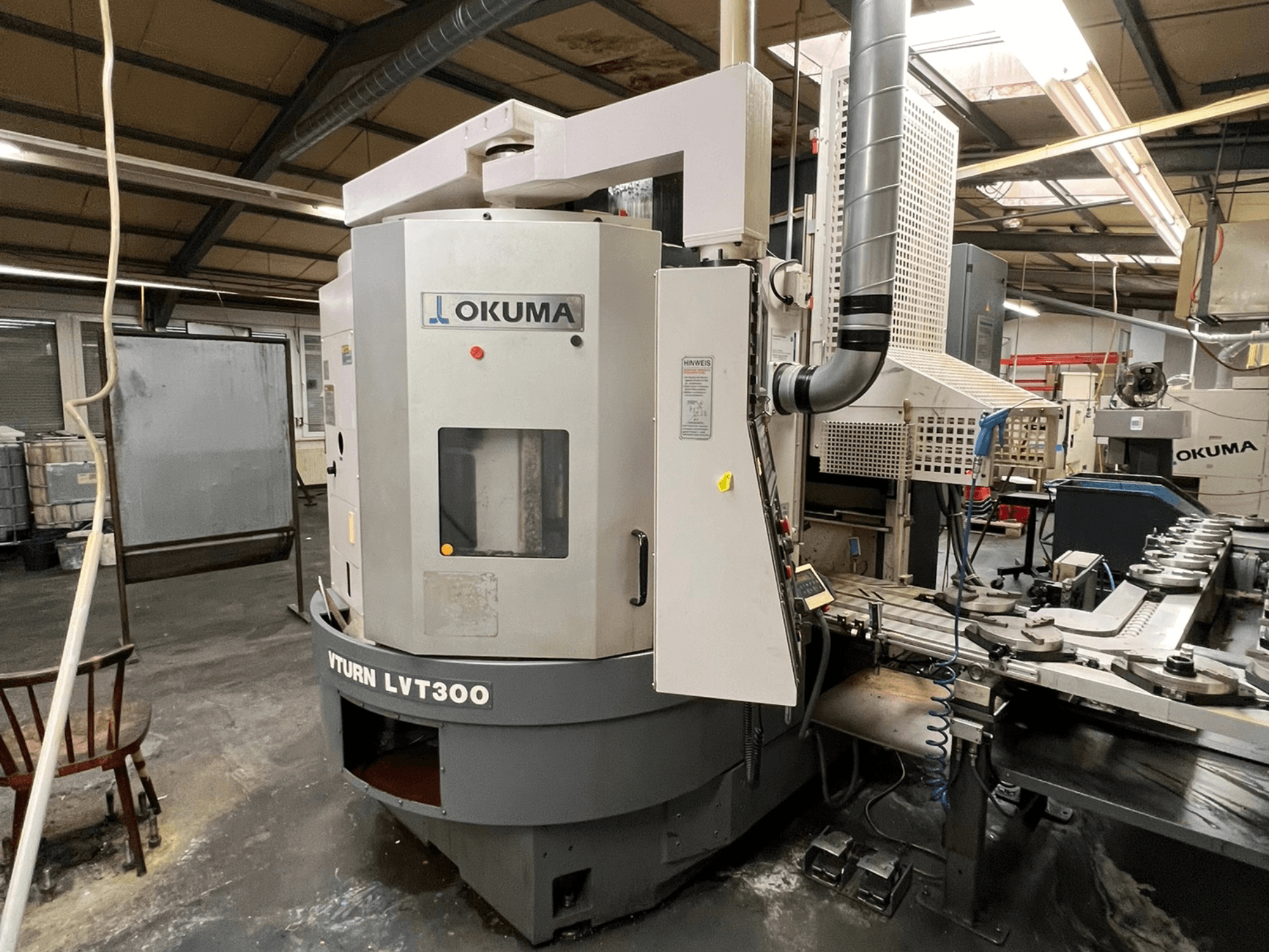 Okuma Vturn LVT300 CNC draaibank, zijaanzicht in industriële omgeving, met het bedieningspaneel en koelsysteem.