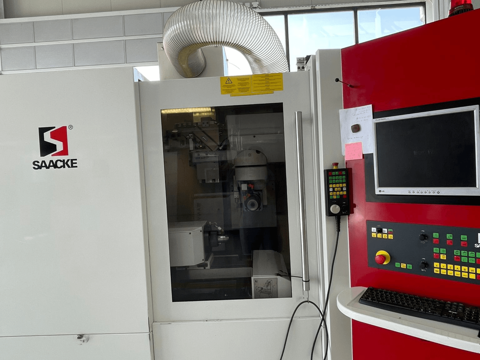 SAACKE machine in wit en rood, vooraanzicht, met bedieningspaneel, monitor en zichtbare interne onderdelen door glas.