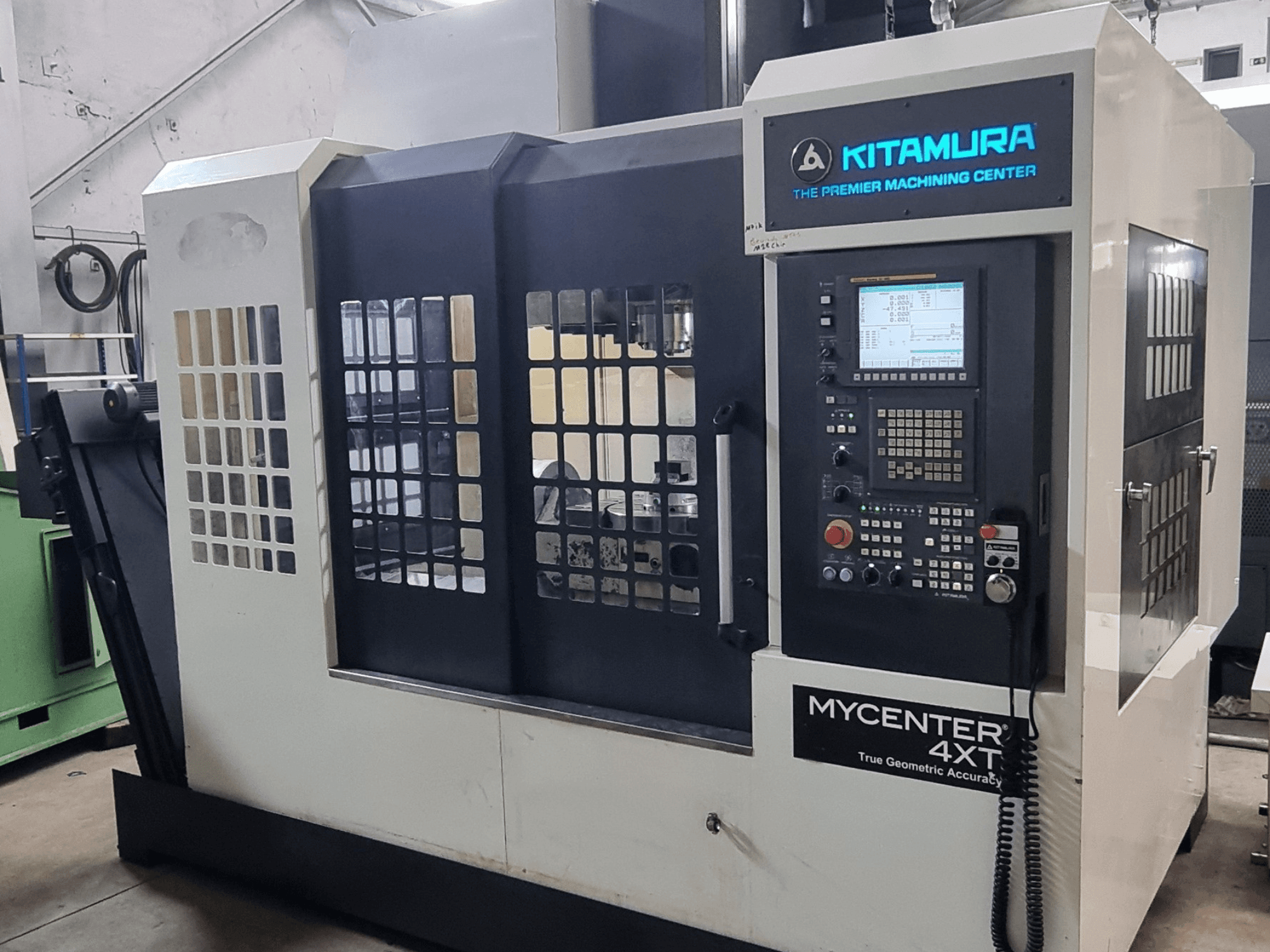 Alternatieve tekst: Kitamura MYCENTER 4XT verticaal bewerkingscentrum, vooraanzicht, met het bedieningspaneel en de machineonderdelen in een werkplaatsomgeving.