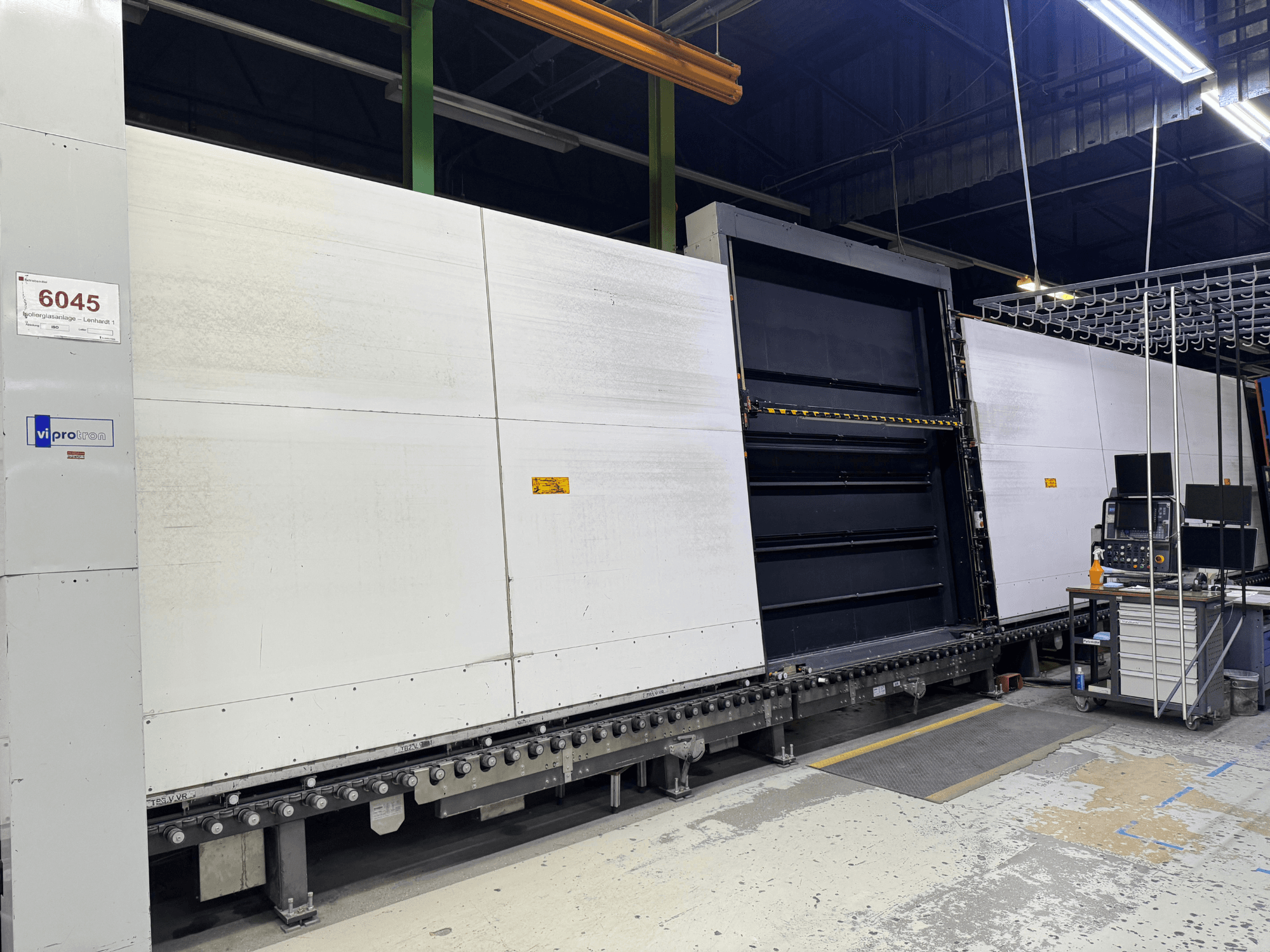 Vooraanzicht van de Vipro matrijsmachine met open paneel, waarop de operationele apparatuur en een werkruimte ernaast te zien zijn. Model 6045.