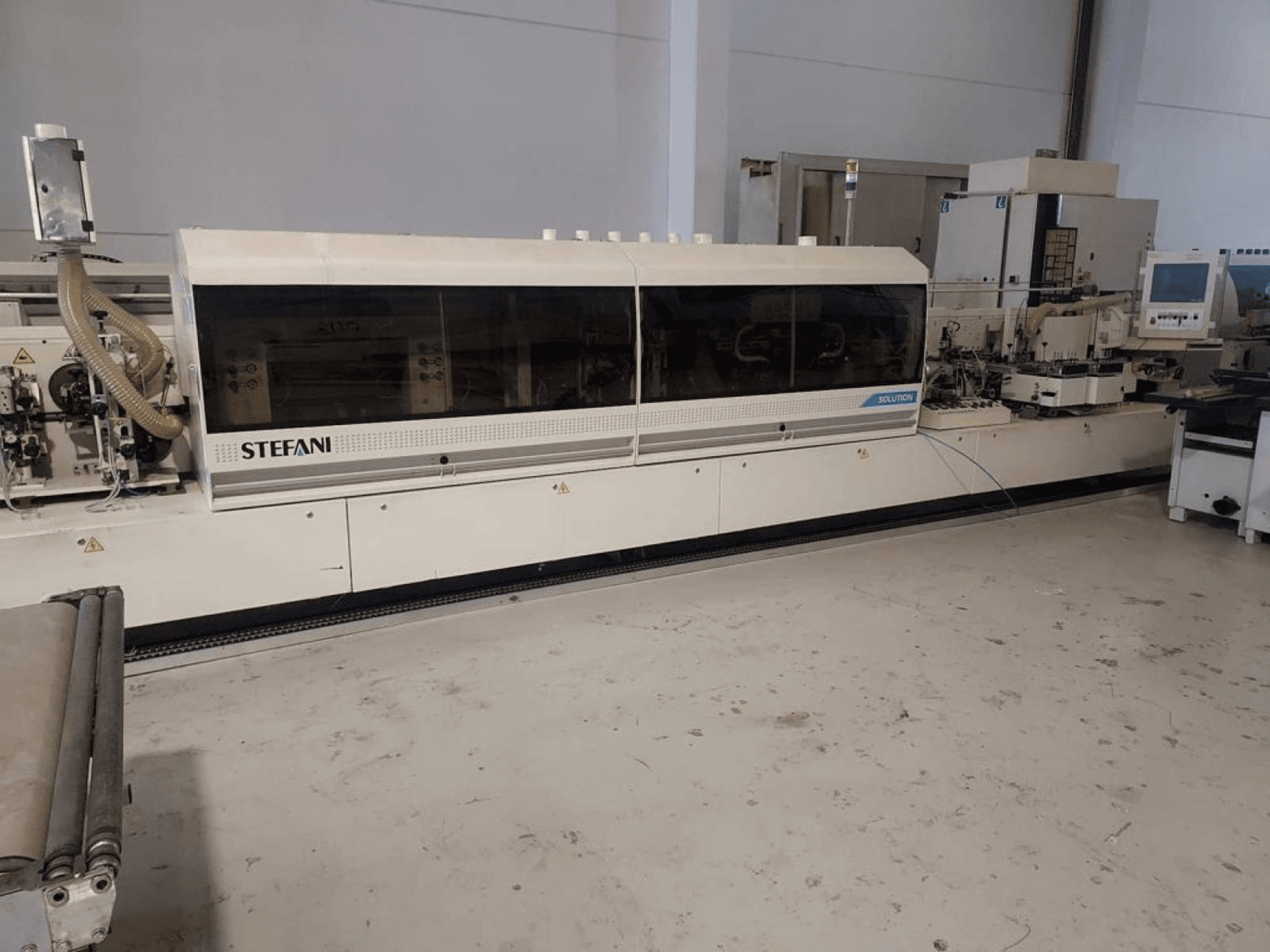 Stefani Solutions kantenaanlijmmachine, vooraanzicht, met stofafzuiging en bedieningspaneel zichtbaar, in een werkplaats.