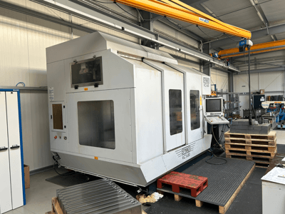 Spinner VC 1650 CNC machine, vooraanzicht, met bedieningspaneel, grote ramen en gestapelde pallets in de buurt in een werkplaats.