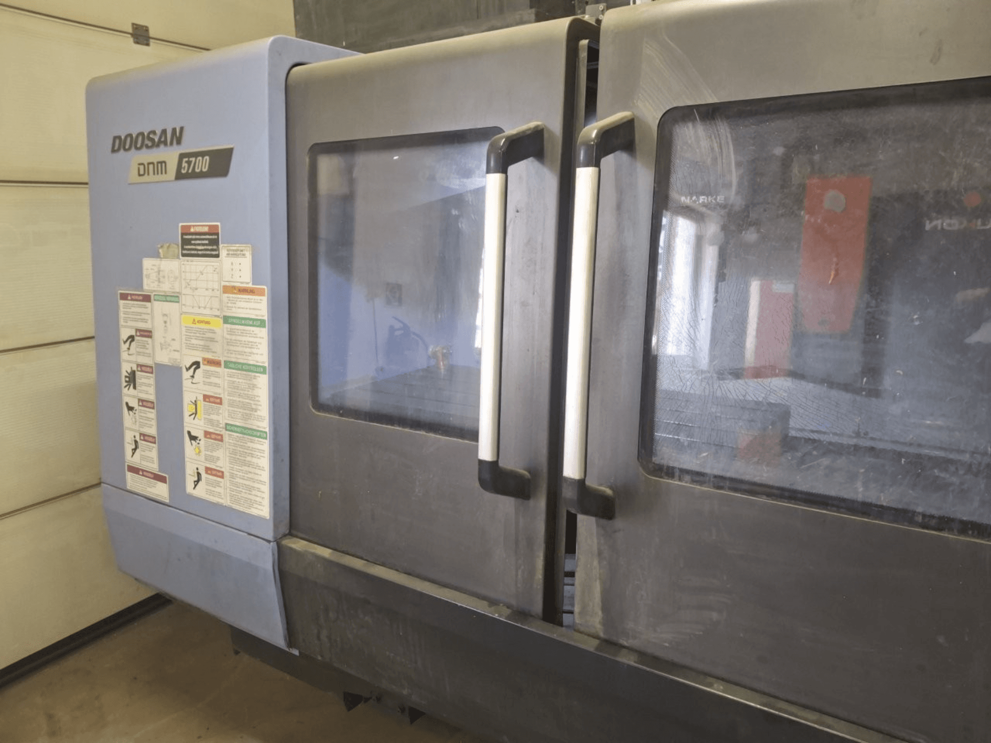 Vooraanzicht van een DOOSAN DNM 5700 verticaal bewerkingscentrum, met dubbele deuren en bedieningspanelen met richtlijnen.