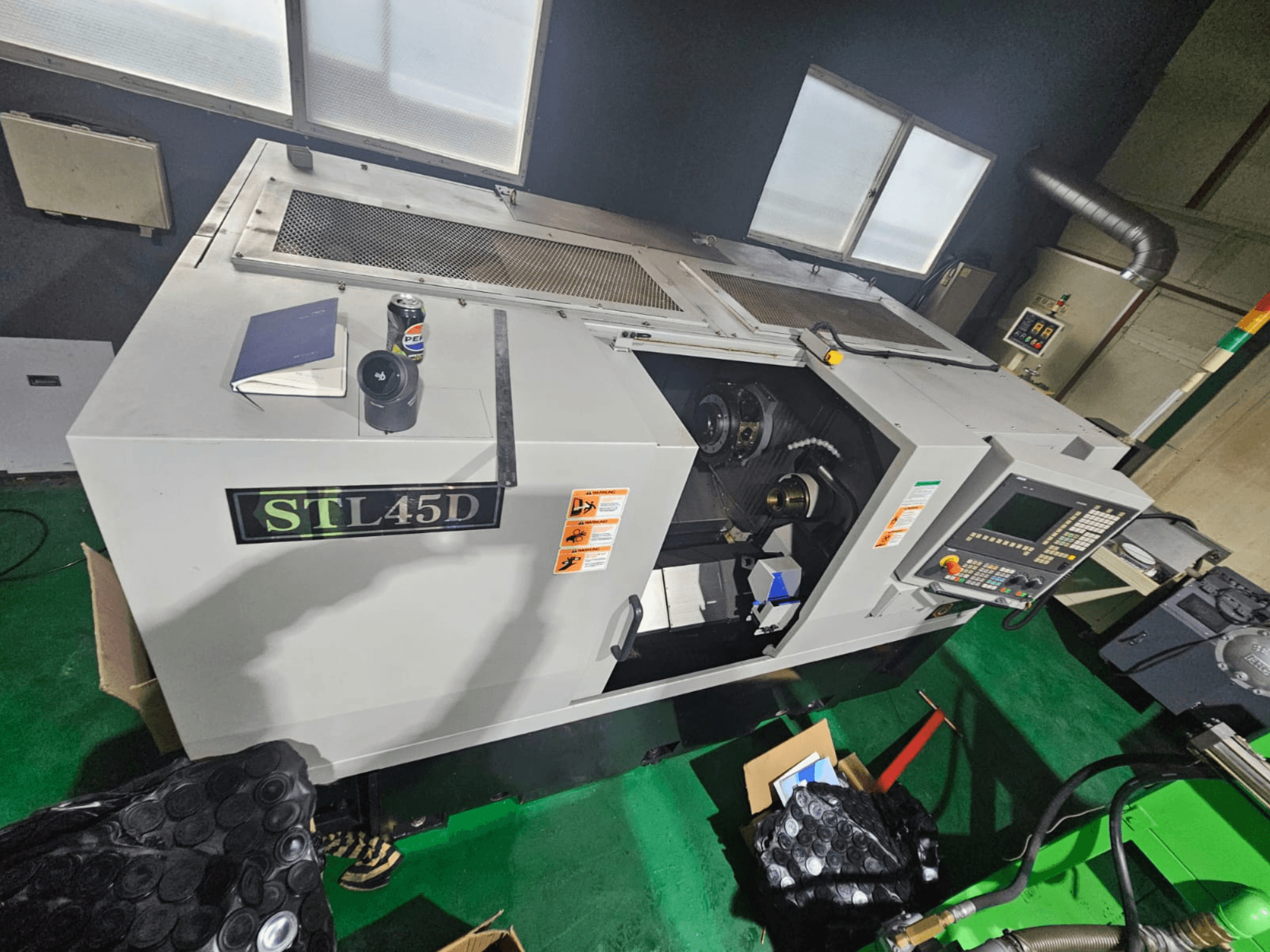 STL45D CNC machine van bovenaf gezien, met bovenaan het bedieningspaneel, cilindrisch onderdeel, notitieblok en blik.