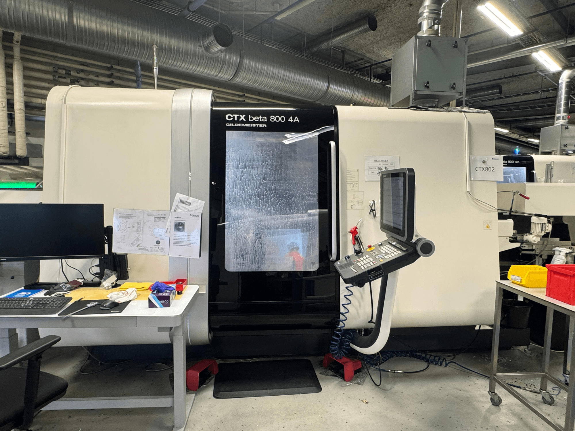 CTX beta 800 4A CNC machine in een werkplaats, zijaanzicht met bedieningspaneel en werkruimte vol gereedschap en documenten.