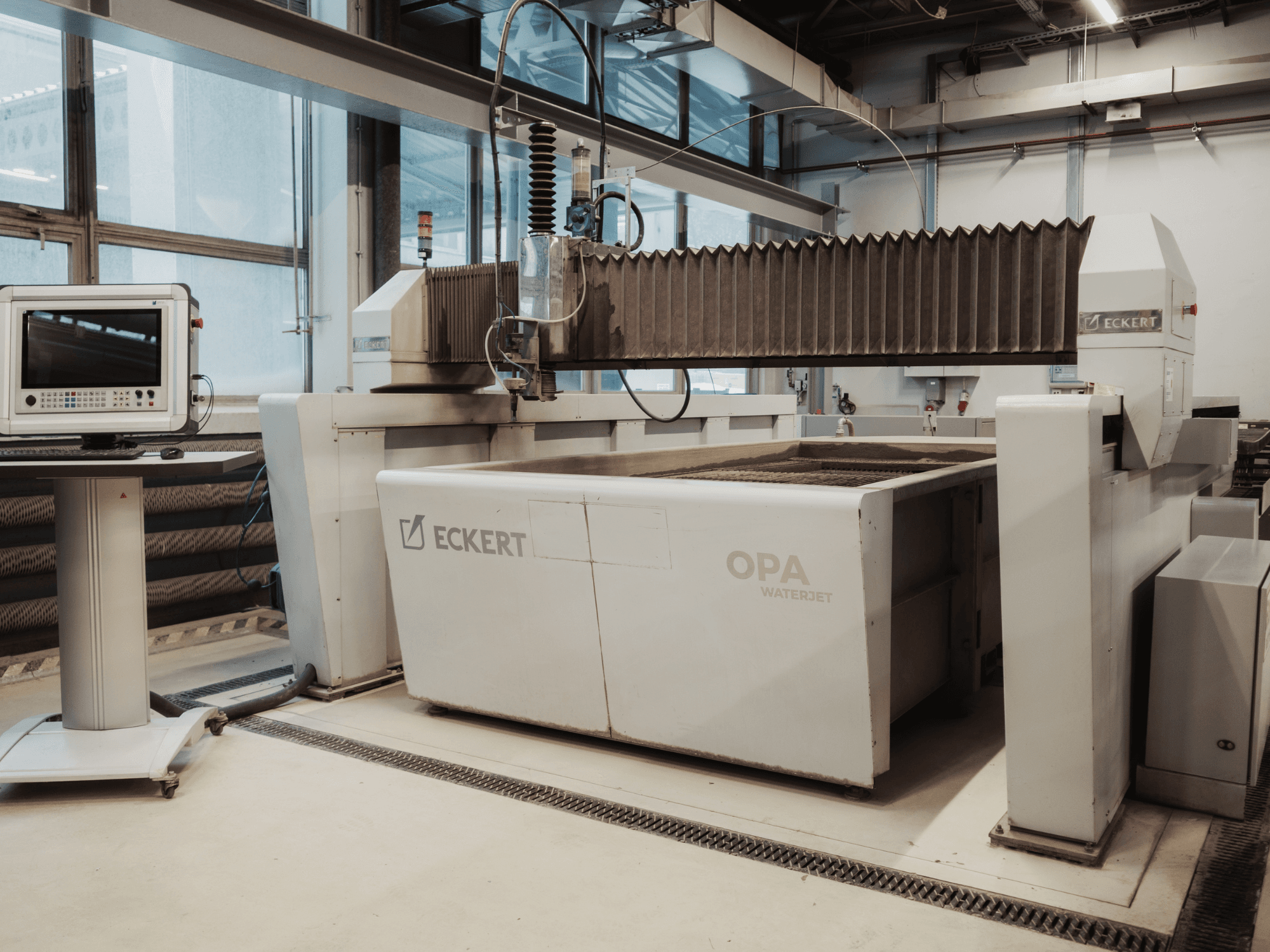 Een ECKERT OPAL-waterstraalsnijmachine in een werkplaats, gezien vanaf de voorkant met het bedieningspaneel ernaast.