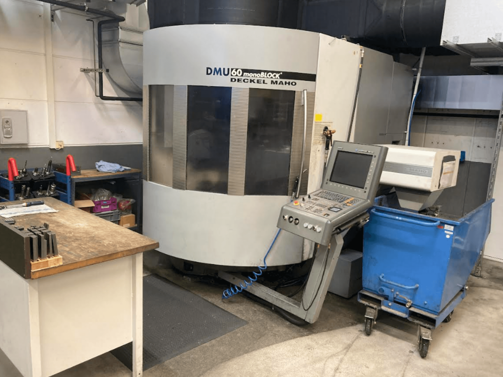 DMG MORI DMU 60 Monoblock verticaal bewerkingscentrum, vooraanzicht met bedieningspaneel, werkruimte en blauwe gereedschapswagen zichtbaar.