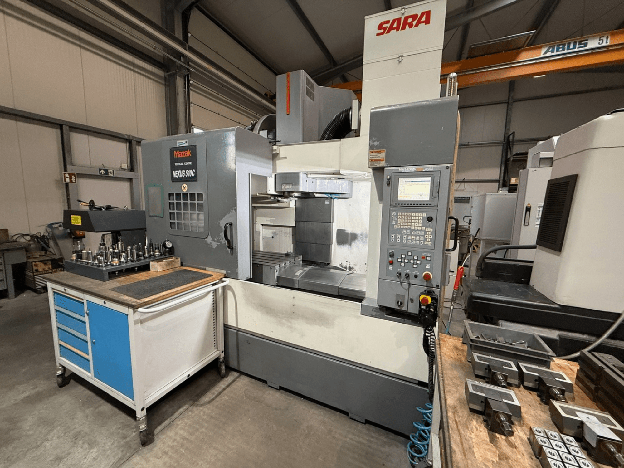 Mazak Nexus 510C verticaal bewerkingscentrum, vooraanzicht, met gereedschappen op een kar; SARA-logo zichtbaar; technische bedieningselementen getoond.