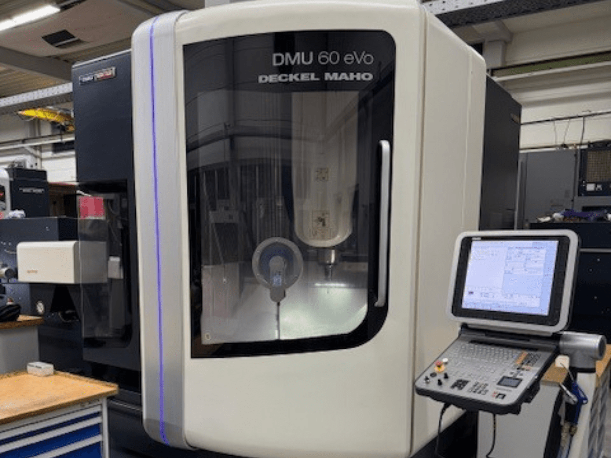 DMU 60 eVo van DECKEL MAHO, vooraanzicht van CNC freesmachine met bedieningspaneel en beeldscherm, waarop precisiecomponenten te zien zijn.