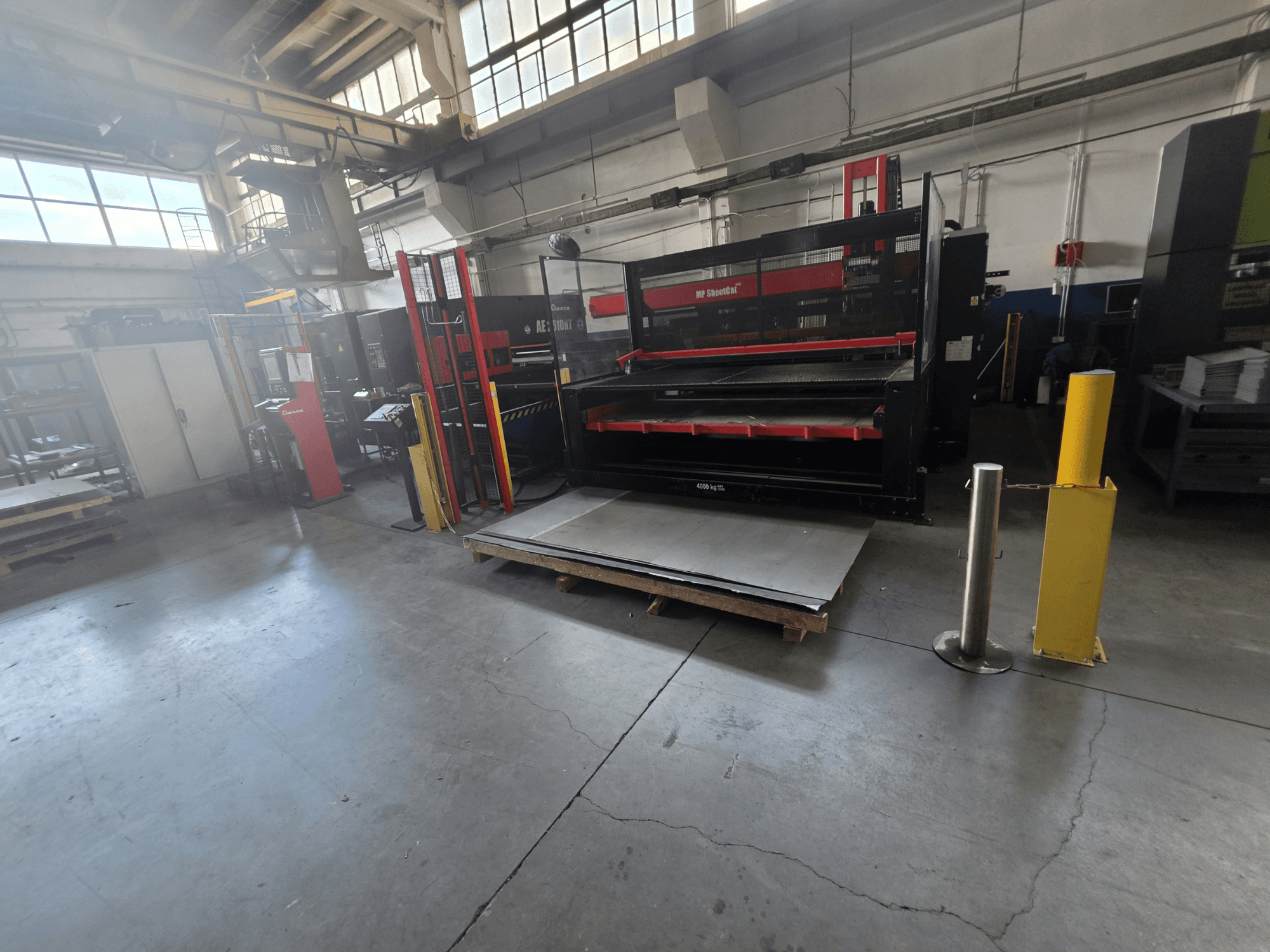CNC-ponsmachine AMADA AE-2510NT in het magazijn, gezien vanuit een zijdelingse hoek, met de opstelling van de machine en de metalen platen.