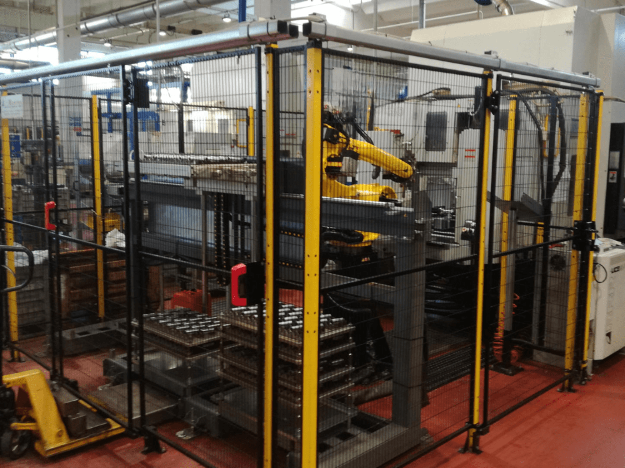 Enshu EV450 verticaal bewerkingscentrum in een omheinde werkruimte, met robotarmen en meerdere gestapelde werkstukken. Vooraanzicht.