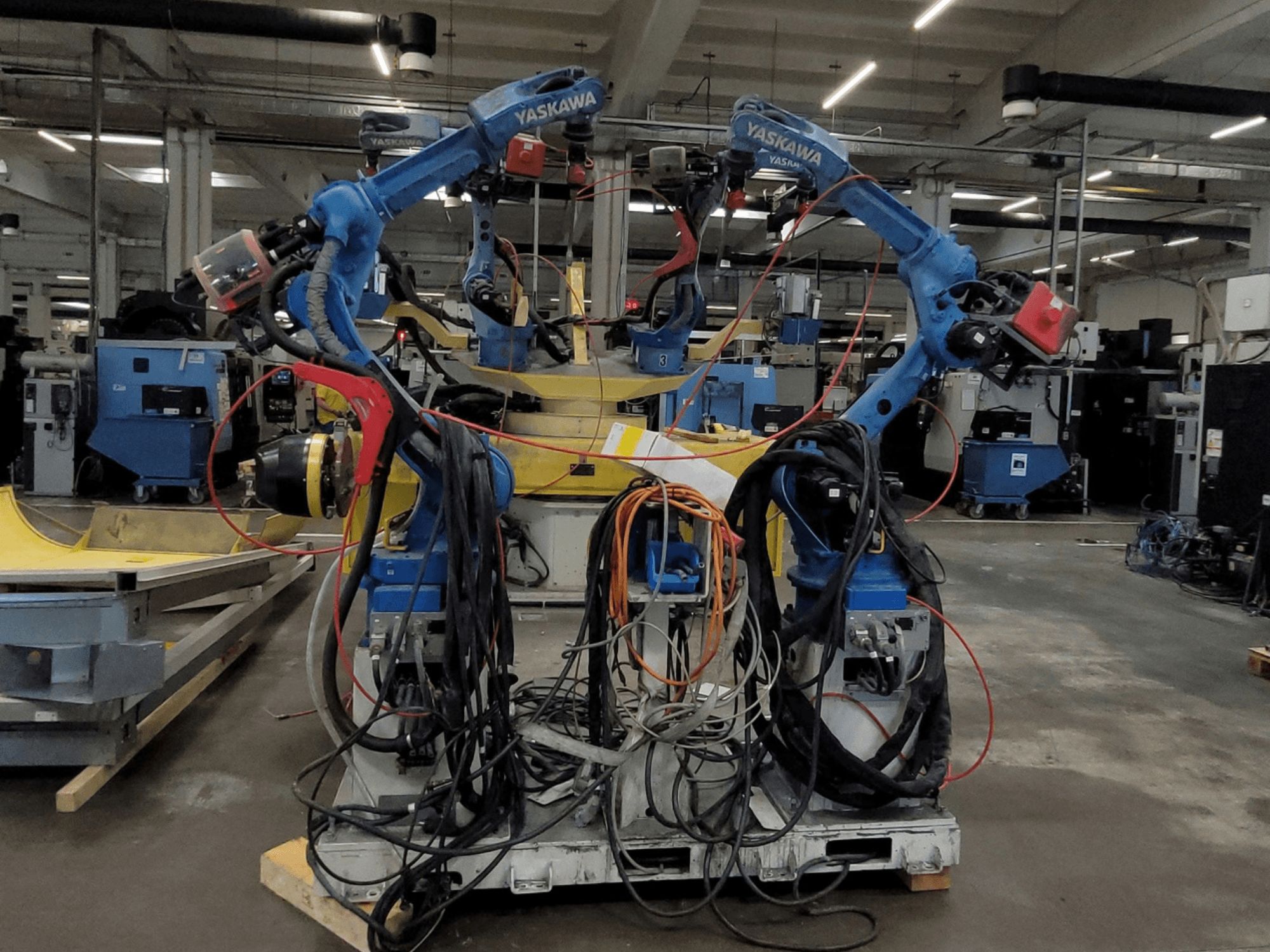 Yaskawa-lasrobotcel RWC L1_OS 15330, vooraanzicht, met twee blauwe robots, voorzien van uitgebreide bekabeling en lasgereedschap.