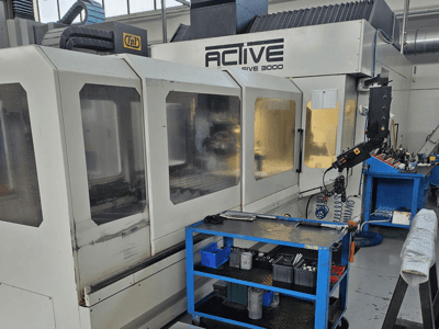 Actieve 3000 CNC machine in een werkplaats, vooraanzicht met gereedschappen op een blauwe kar, zichtbare bedieningselementen en werkgebied binnenin.
