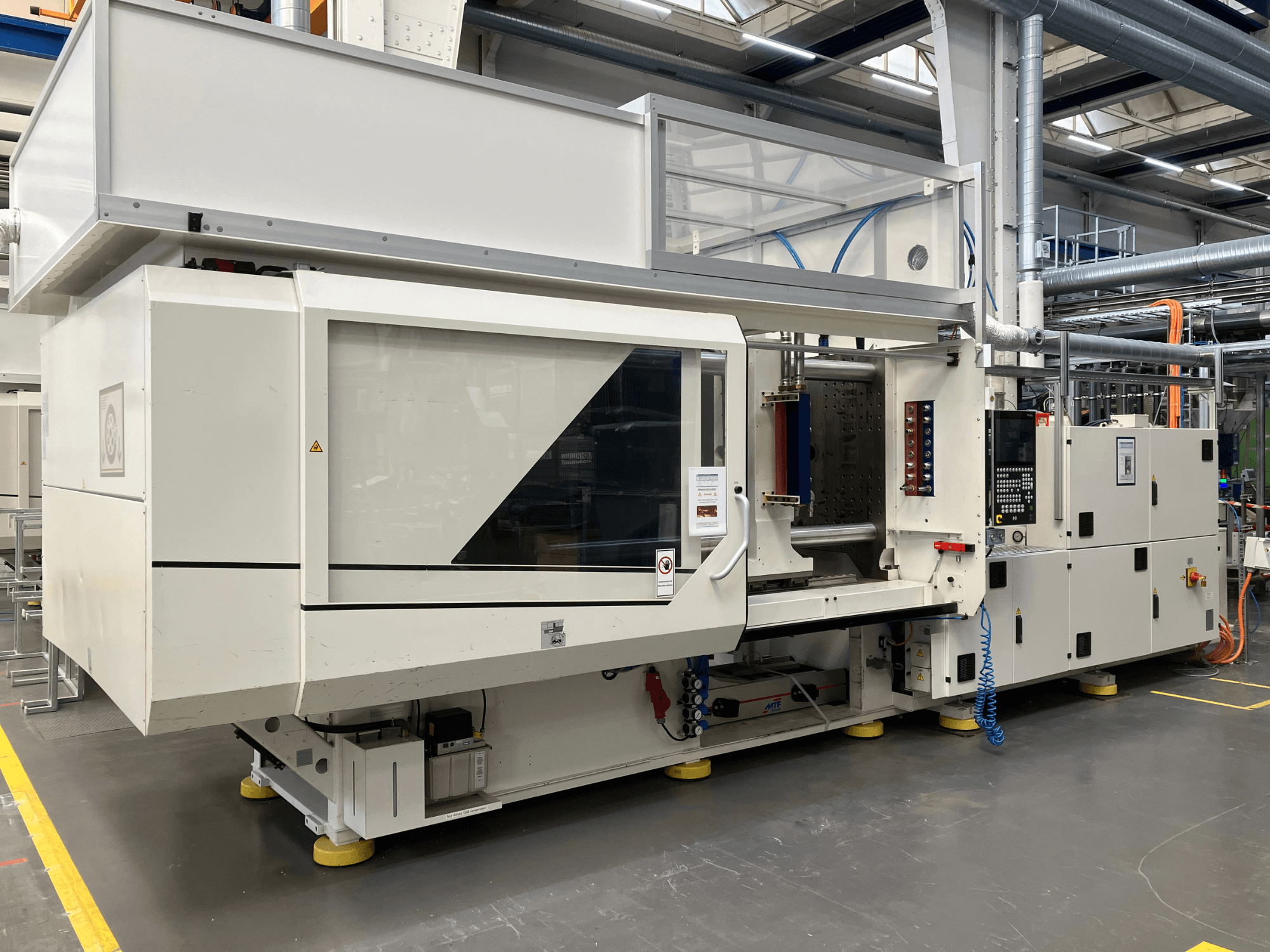 Zijaanzicht van een spuitgietmachine, model AET, met bedieningspaneel en transparante afdekkingen, in een industriële omgeving.