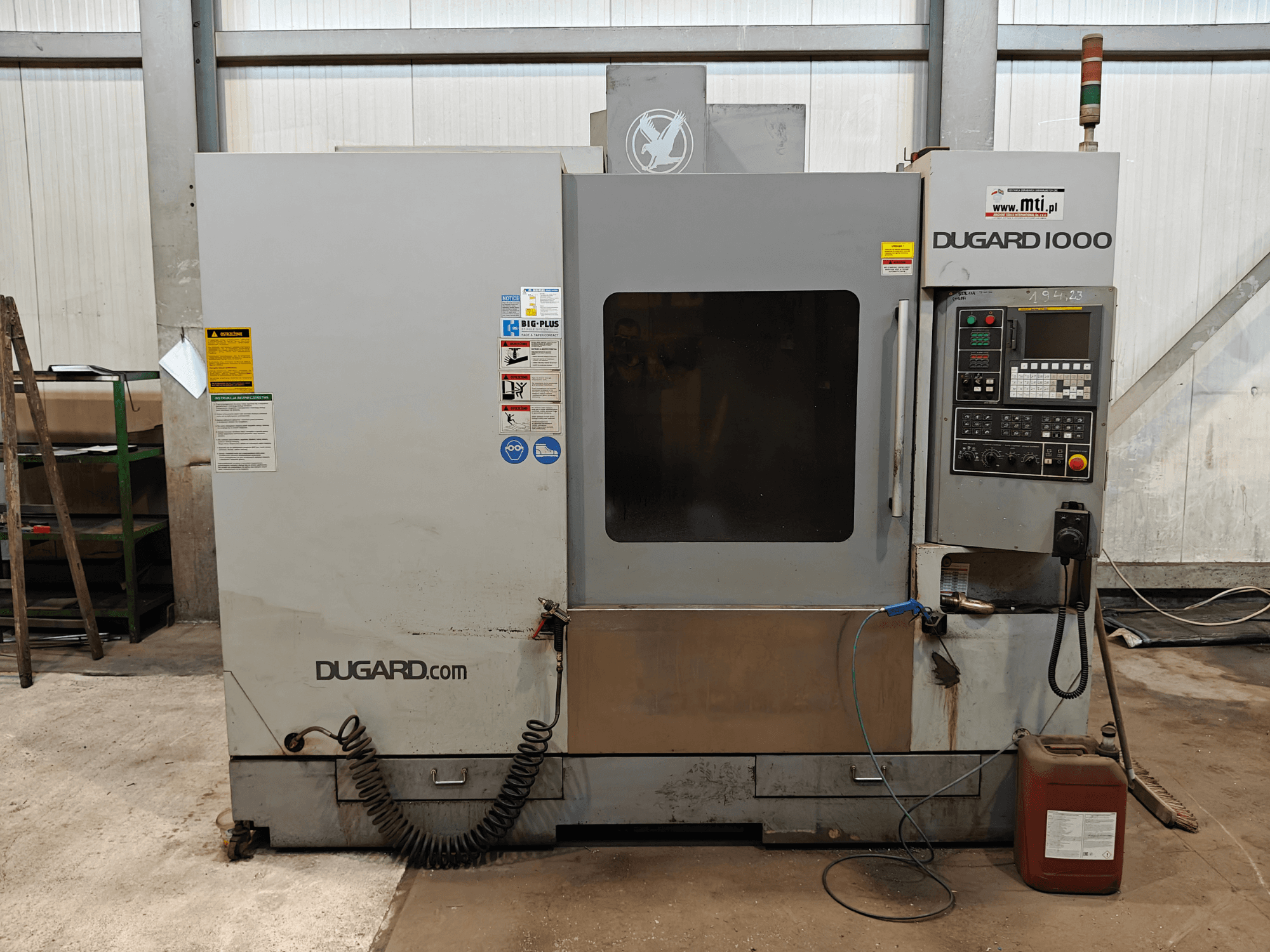 Dugard 1000 CNC machine, vooraanzicht, met bedieningspaneel, veiligheidslabels en oliecontainer, in een werkplaats.