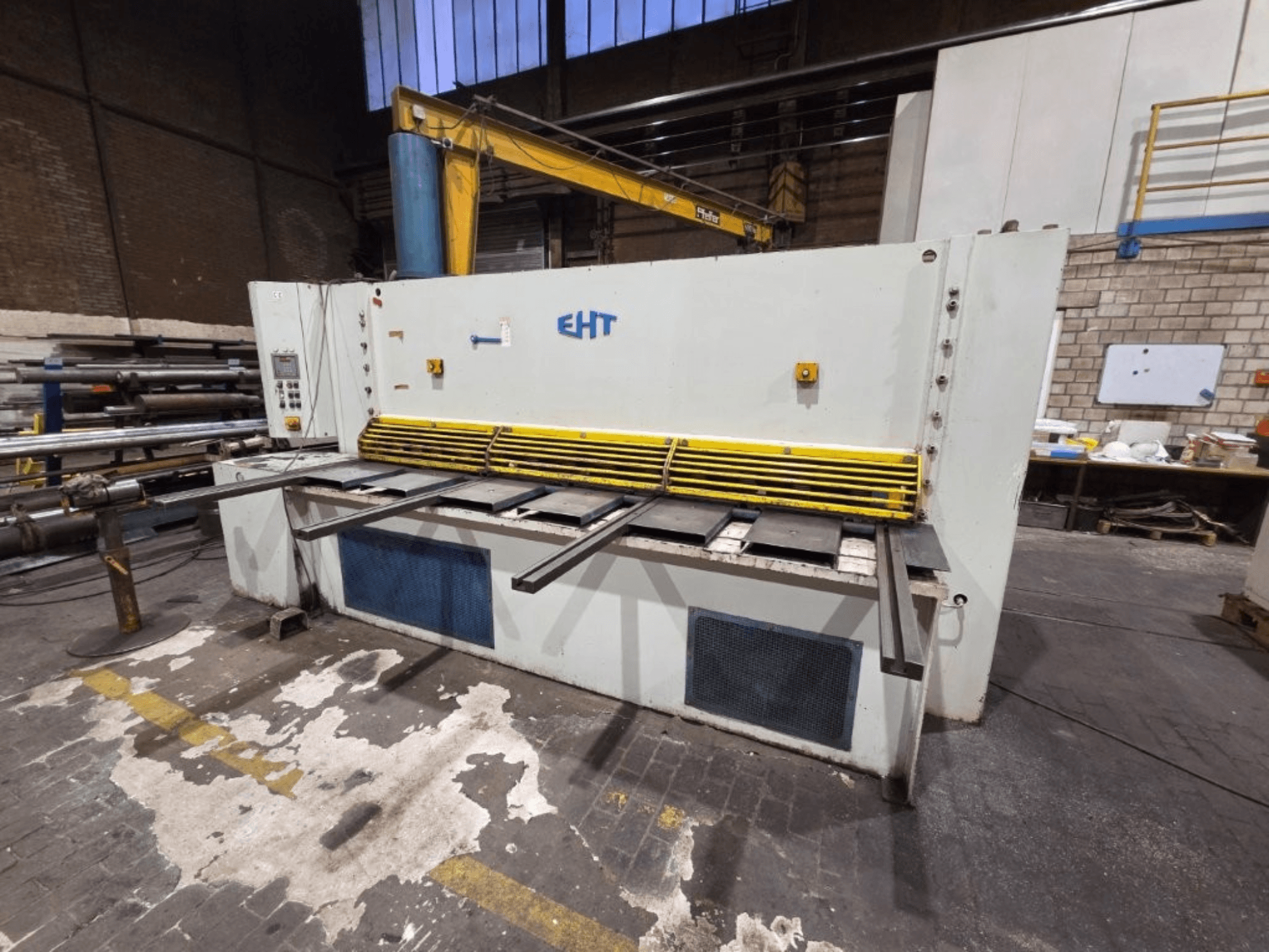 Hydraulische EHT-schaarmachine gezien vanaf de voorkant, met gele veiligheidsafscherming en bedieningspaneel met bedieningselementen.