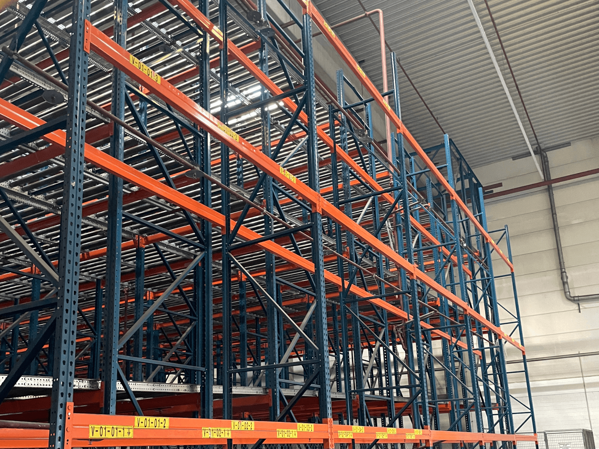 FL SYSTEME F05.10 FLG-palletverwerkingssysteem in een magazijn, zijaanzicht, met zware oranje en blauwe stellingen.