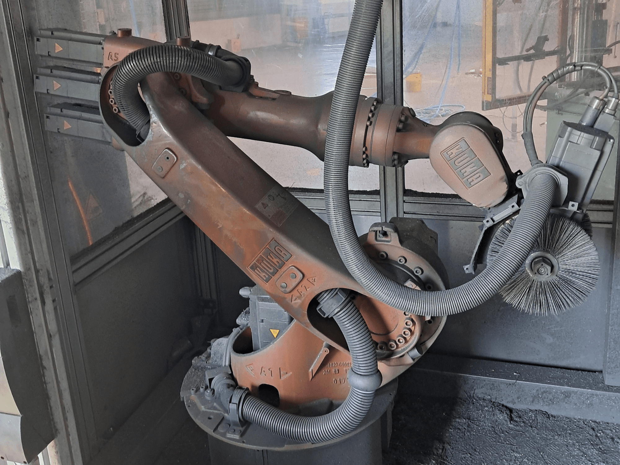 De KUKA KR 16-2-robotarm in zijaanzicht, met zichtbare kabels, borstels en mechanische scharnieren, geplaatst in een werkomgeving.