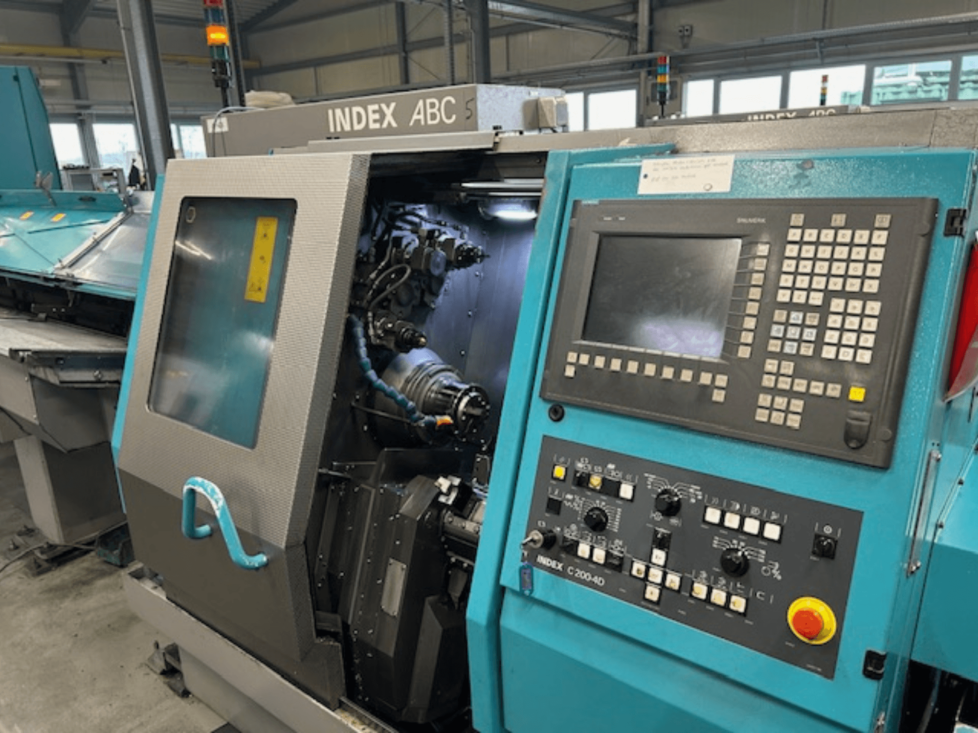Vooraanzicht van een INDEX C200-AD CNC draaibank met bedieningspaneel, zichtbare interne onderdelen en veiligheidsfuncties.