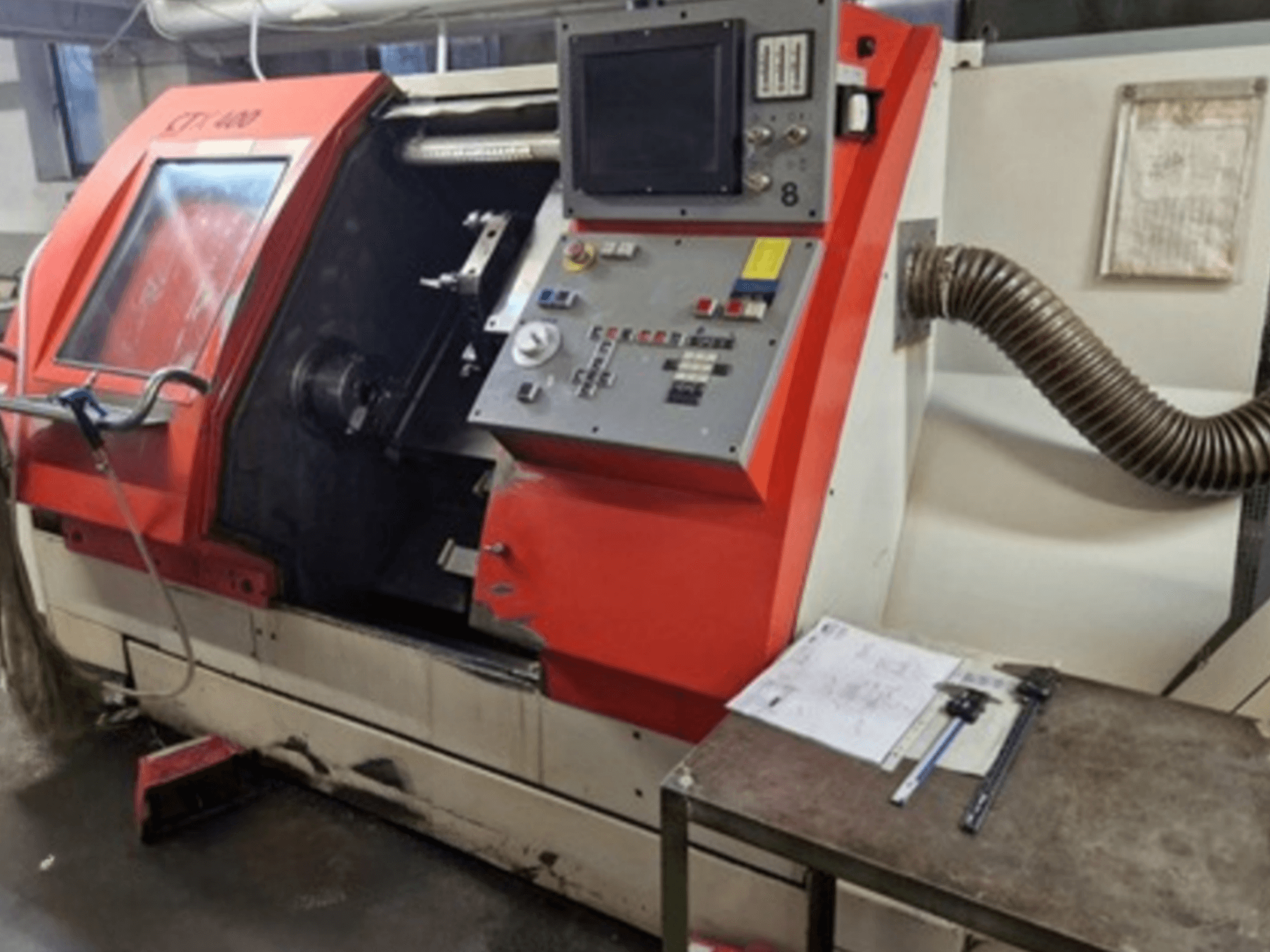 Gildemeister CTX 400 horizontale draaimachine, vooraanzicht met bedieningspaneel en afzuigslang. Inclusief meetgereedschap op tafel.
