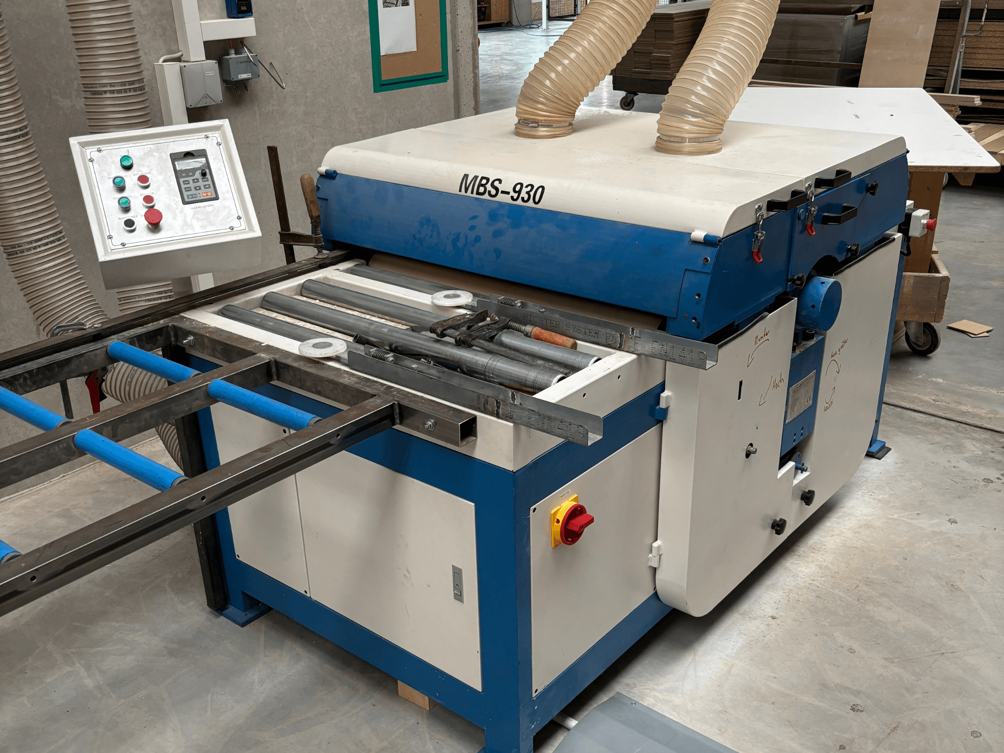 MBS-930 houtbewerkingsmachine met bedieningspaneel en rollen, gezien vanaf de zijkant, met stofafzuigslangen.
