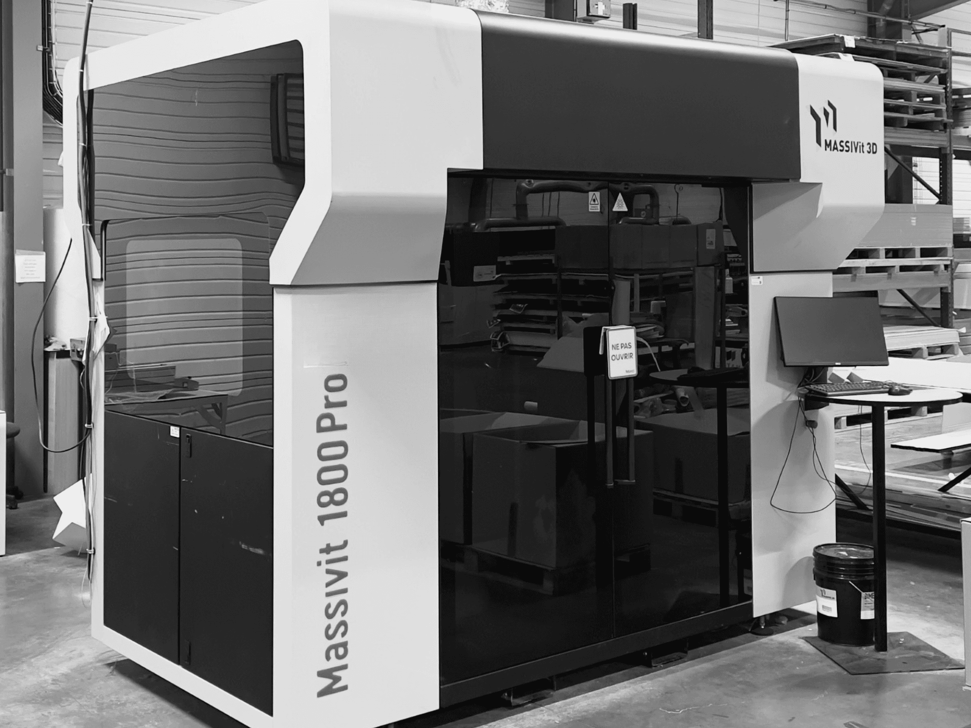 De kunststof 3D-printer MASSIVIT 1800 PRO in een werkplaats, vooraanzicht, met een computerwerkplek en bedieningspaneel in beeld.