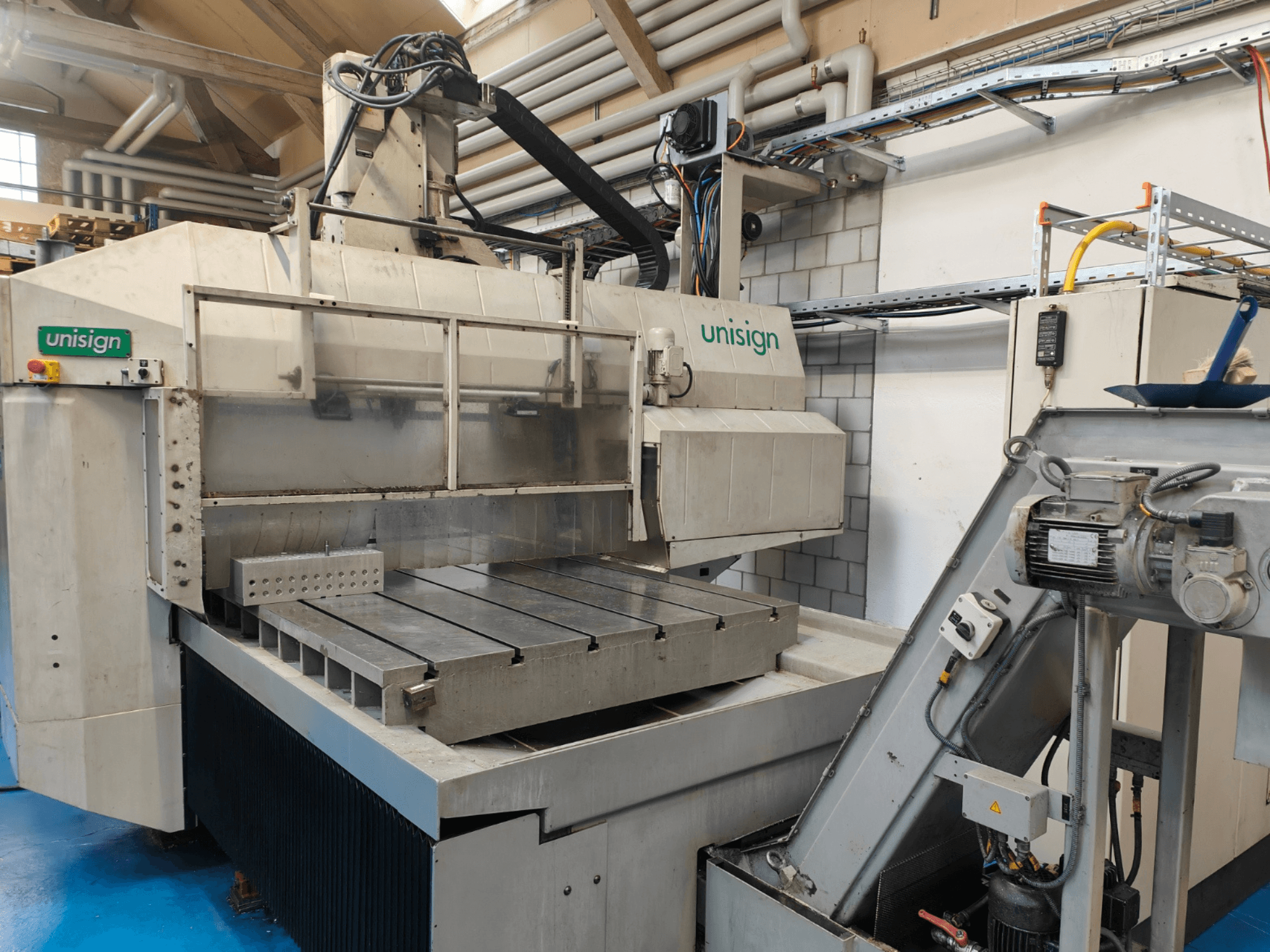 Unisign CNC machine in een werkplaats, vooraanzicht, met een grote tafel, bedieningspaneel en industriële ontwerpelementen.